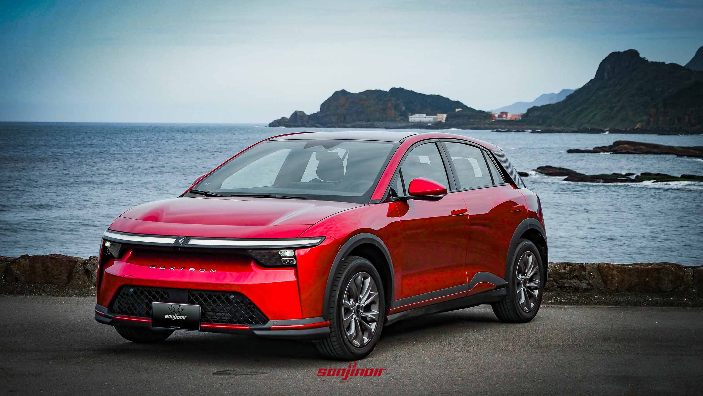 紅色Foxtron Bria Emerge停放在海岸旁的左前側視角照片。