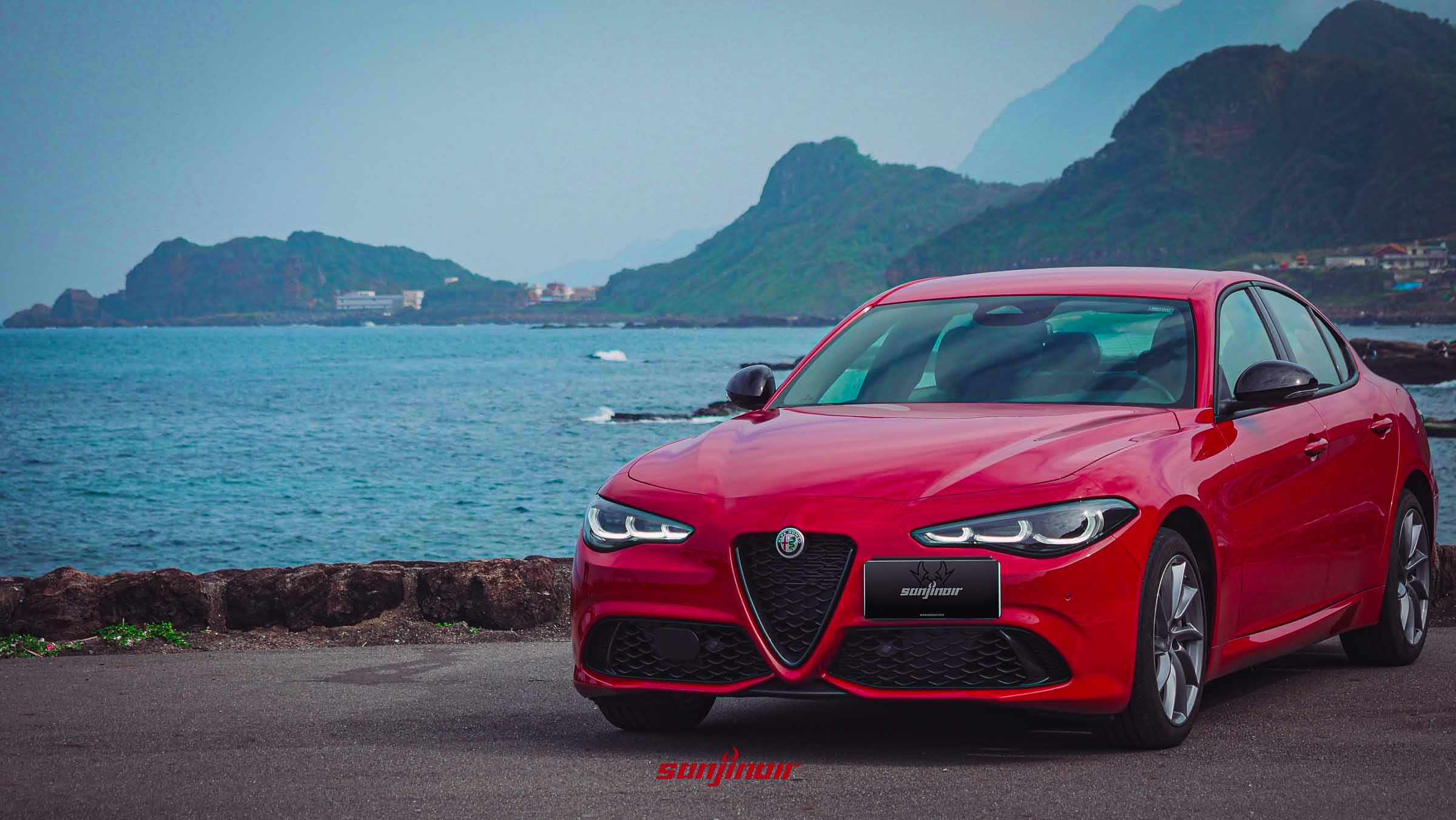 Alfa Romeo Giulia Sprint紅色轎跑車停駐於海岸公路，背景為山脈與海景。
