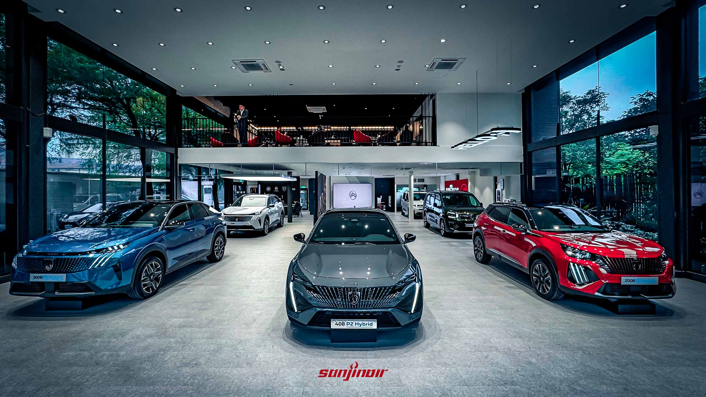 一個光線明亮的汽車展廳，灰色瓷磚地板，天花板有射燈和大型玻璃幕牆。多輛汽車排列整齊。左前是藍色 PEUGEOT 3008 P2 Hybrid，中間是灰色 PEUGEOT 408 P2 Hybrid，右前是紅色 PEUGEOT 2008 P2 Hybrid。