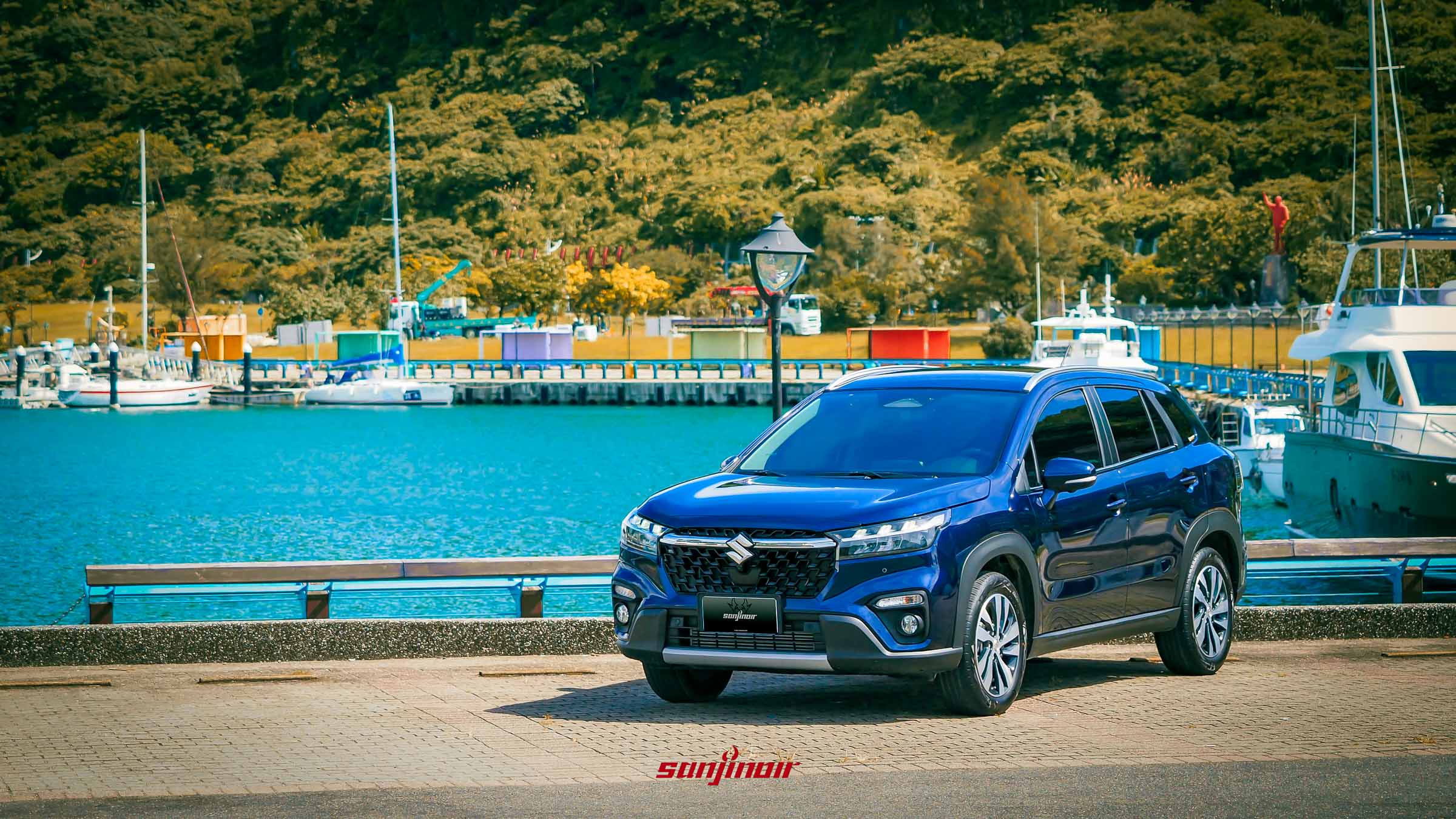 藍色2026年式SUZUKI S-Cross Allgrip停在碼頭前，背景有遊艇與綠色山丘。