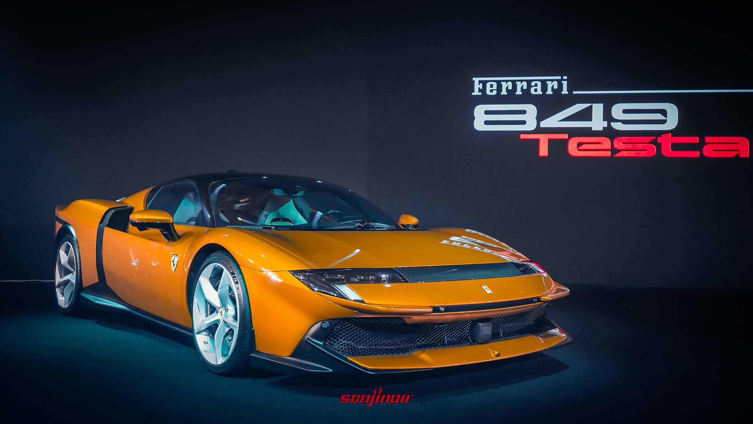 2026 Ferrari 849 Testarossa 橙色插電式混合動力Berlinetta車型在發表會舞台上呈現，燈光聚焦。車款正視角，背後的巨幅螢幕顯示著「Ferrari 849 Testarossa」字樣。