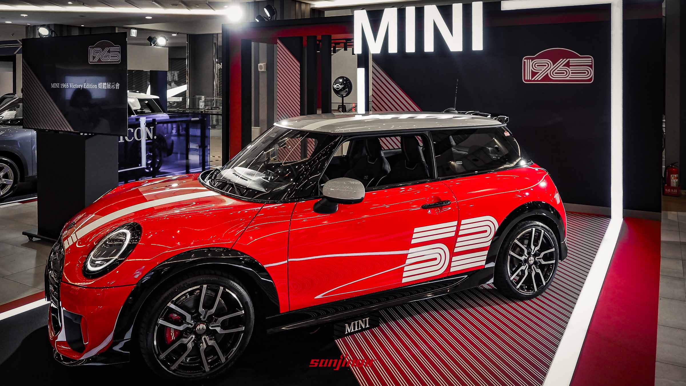一輛紅底白頂的MINI 1965 Victory Edition停放在展示台上，車側印有白色的52號圖騰。