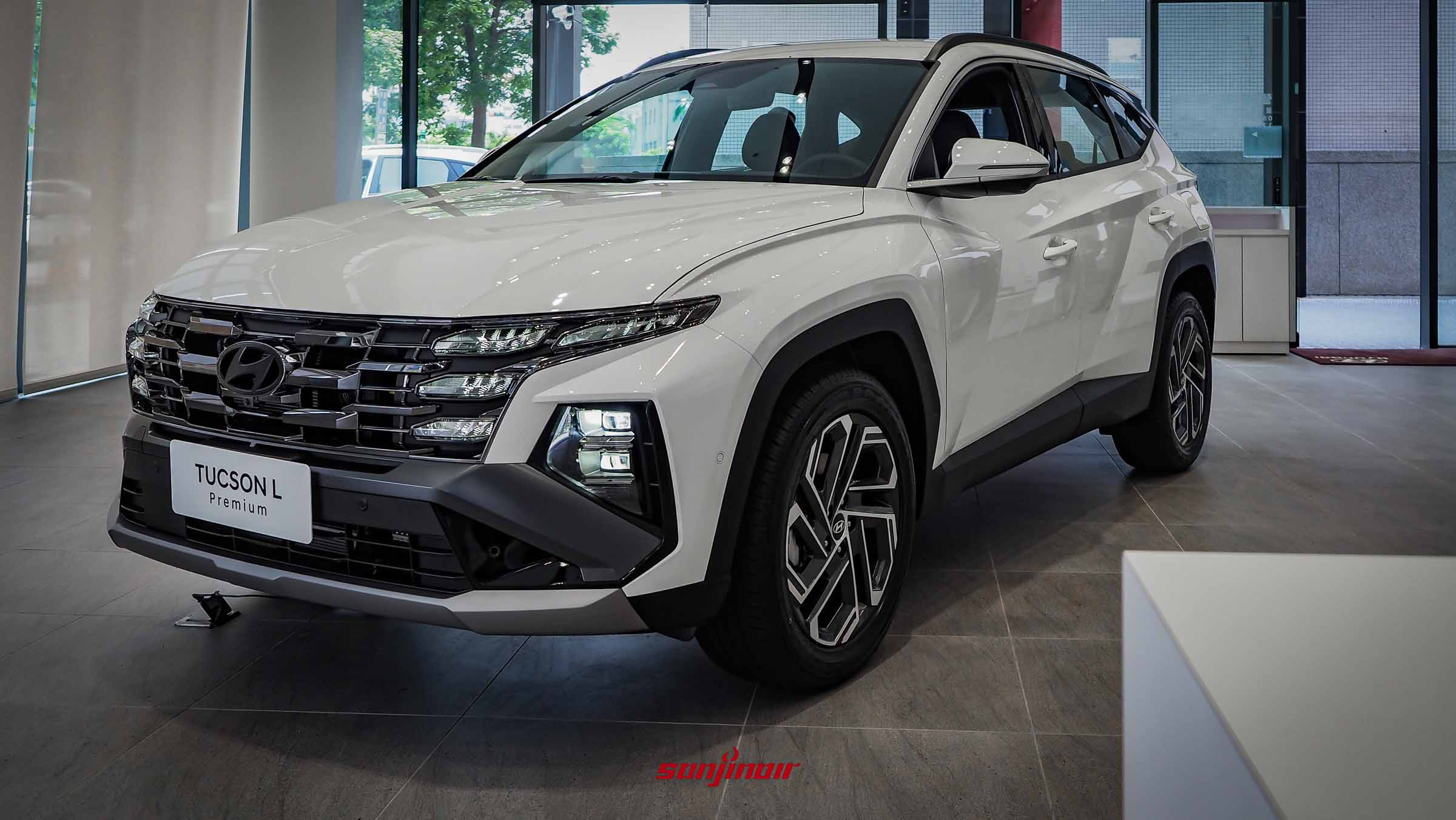 展示於展間內的白色2026 HYUNDAI Tucson L 26.5年式Premium休旅車前方斜側面照，呈現出鑽石黑化水箱護罩與幾何線條輪拱。