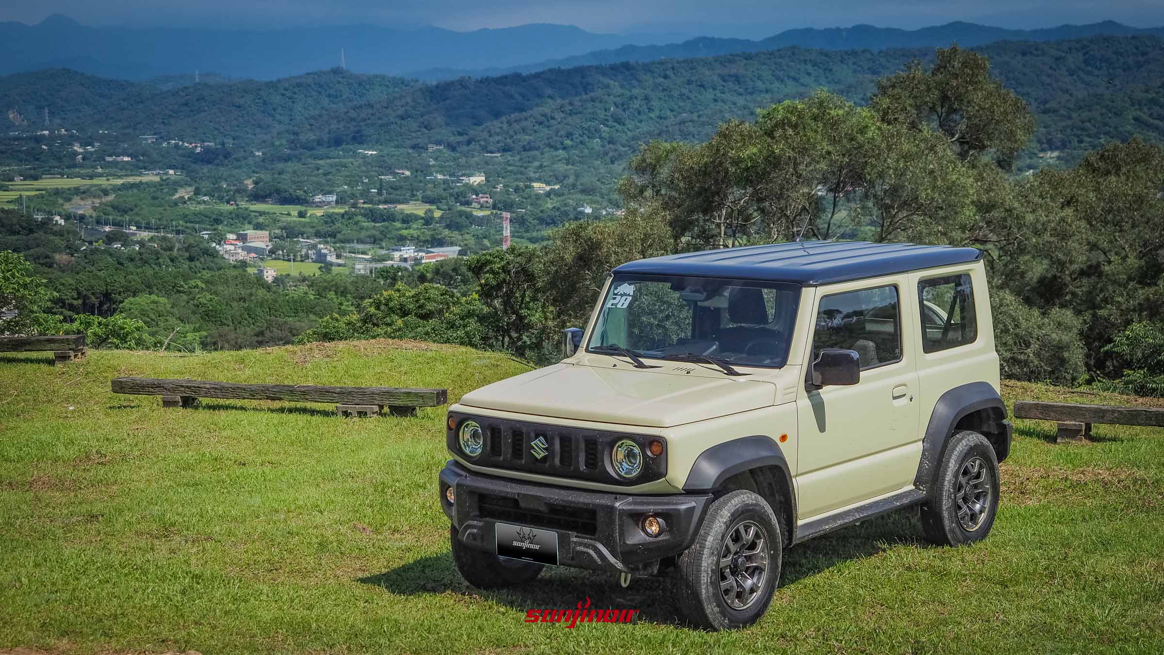 停放於綠色草地上的米色2026年式SUZUKI Jimny前方斜角照。