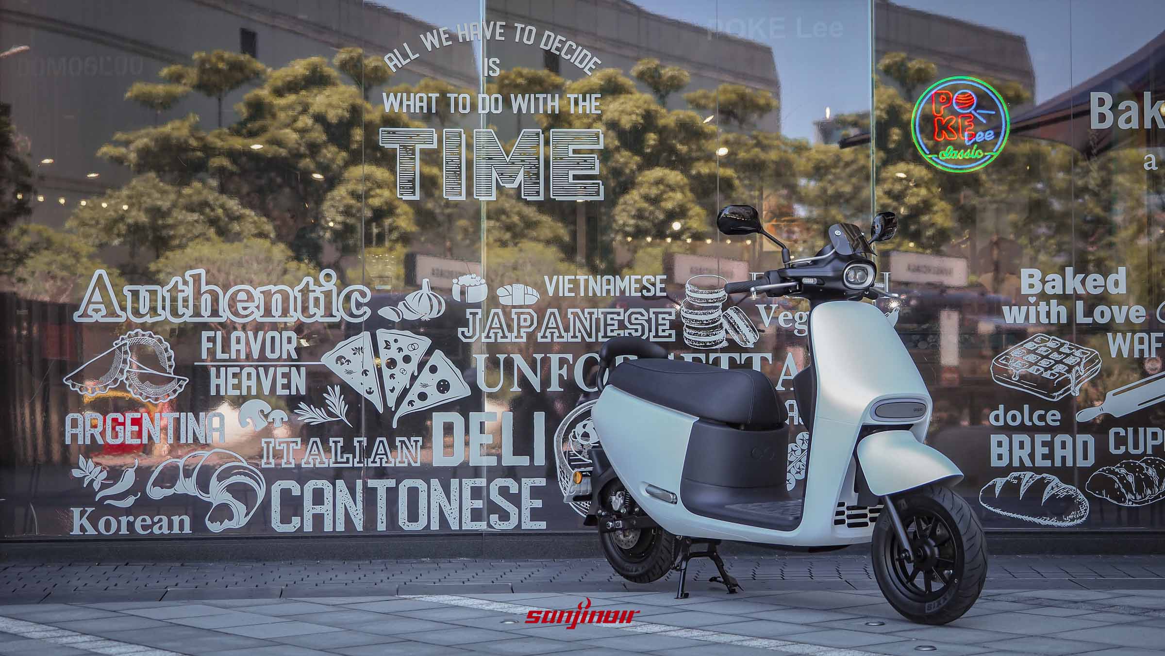 霧面銀白色Gogoro Luna電動機車停在玻璃幕牆前，玻璃上飾有Poke Lee霓虹燈與AUTHENTic、Bake the World等文字塗鴉。