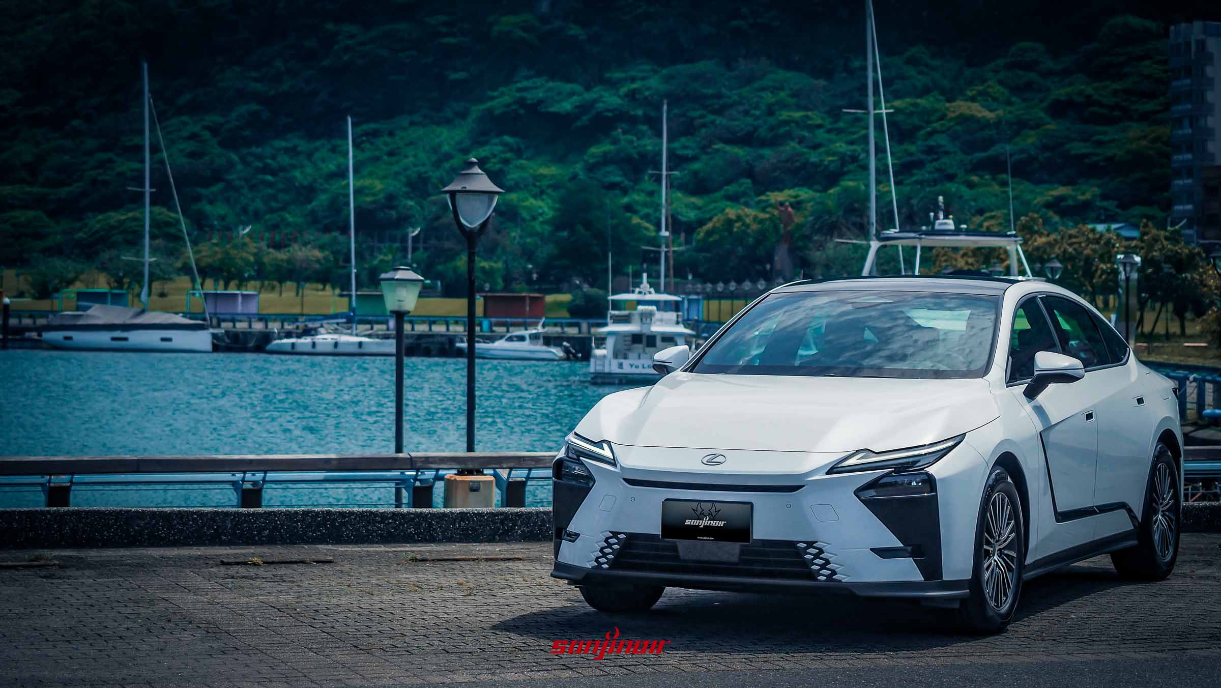 一輛白色的Lexus ES 300h停在碼頭邊，背景有蔚藍的海水、遊艇與綠色山丘。