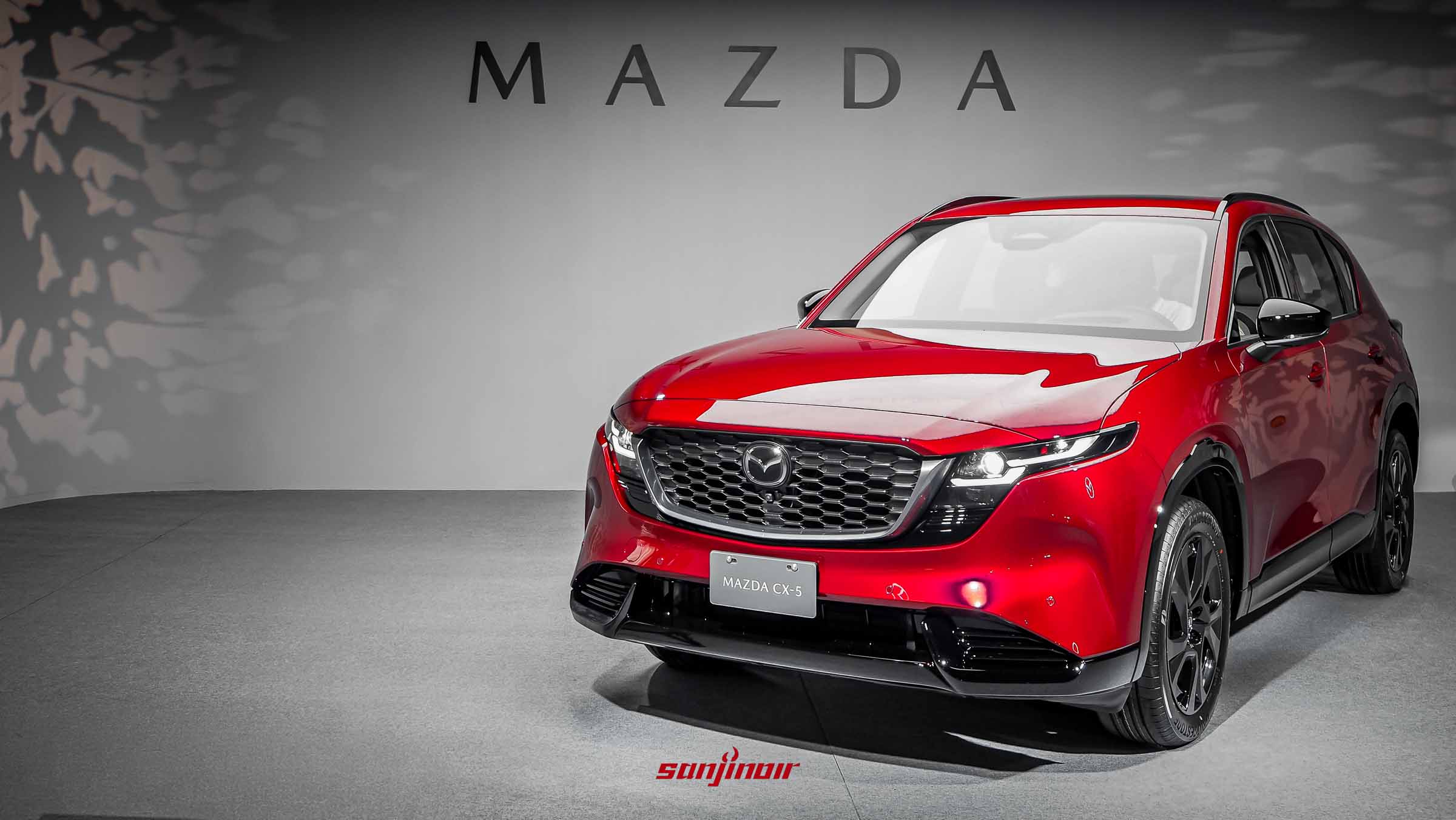 一輛紅色的第三代MAZDA CX-5停放在灰色背景的展示間內，車頭朝向右前方，牆上印有MAZDA字樣。