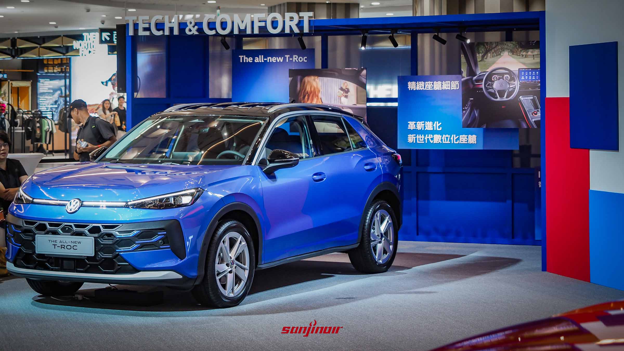 停放在室內展區的藍色 2026 Volkswagen T-Roc 280 eTSI Style Design 正面與側面視角，背景有「TECH & COMFORT」與車室內裝的宣傳看板。
