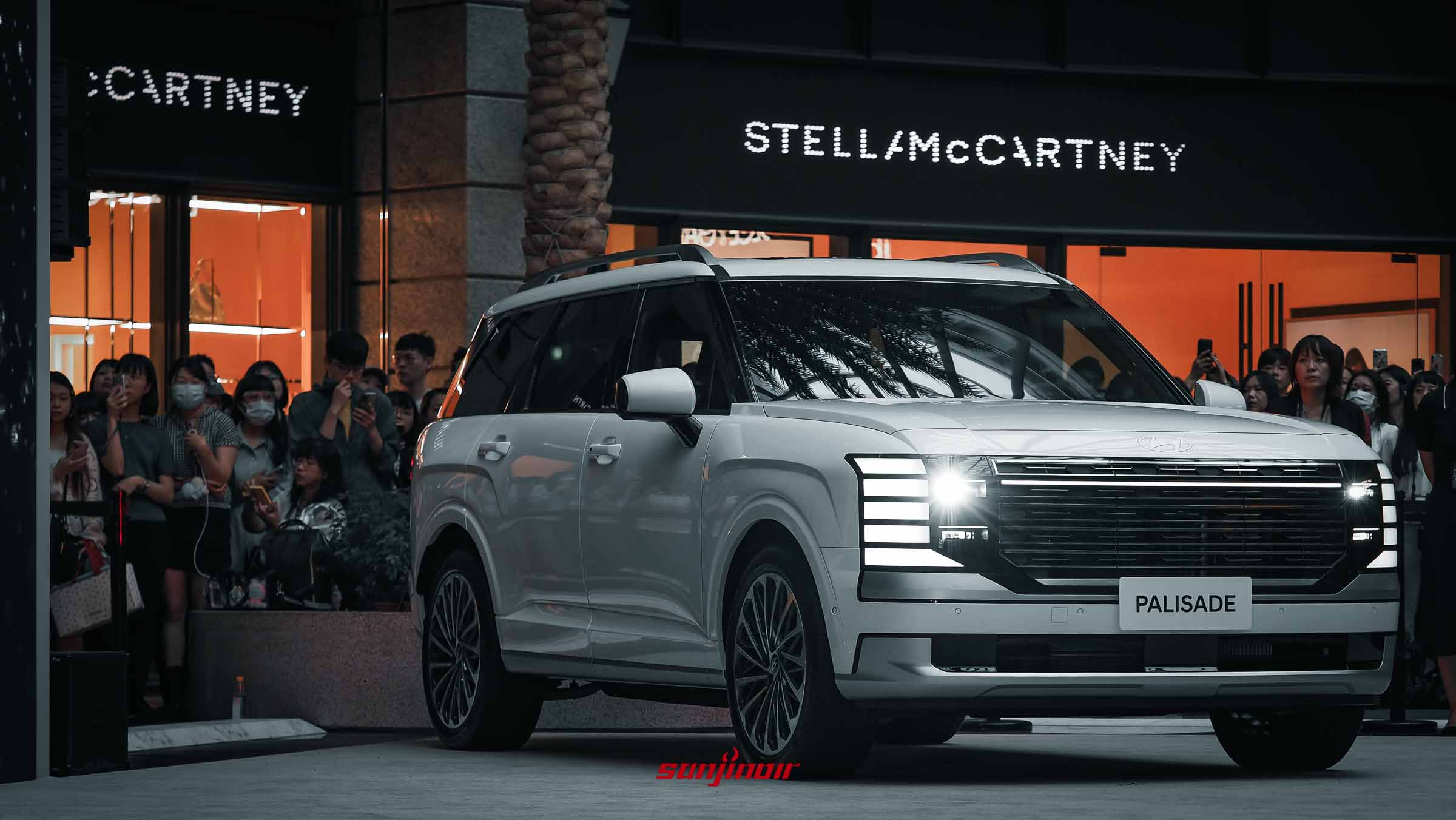 一輛白色的2026 Hyundai Palisade停放在發表會現場，右前方車頭外觀特寫，背景有許多圍觀與拍照的群眾。