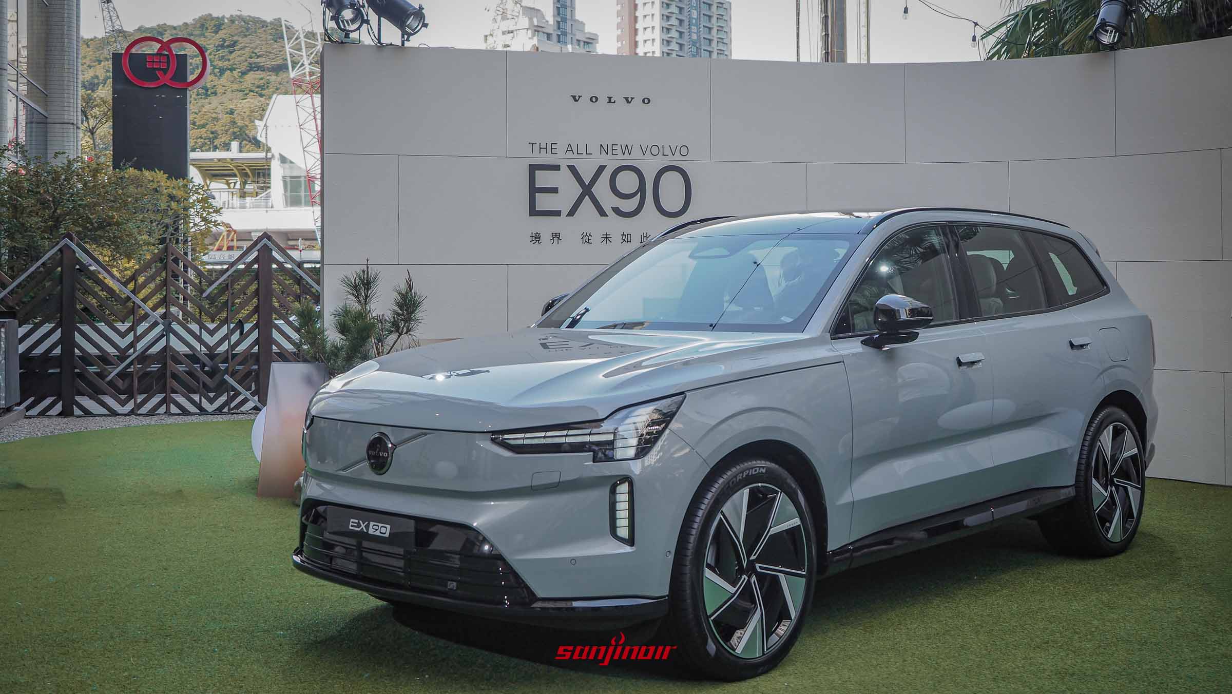 一輛灰色的Volvo EX90純電休旅車停放在人工草皮上，後方有著寫有「THE ALL NEW VOLVO EX90 境界 從未如此智在」的白色背板。