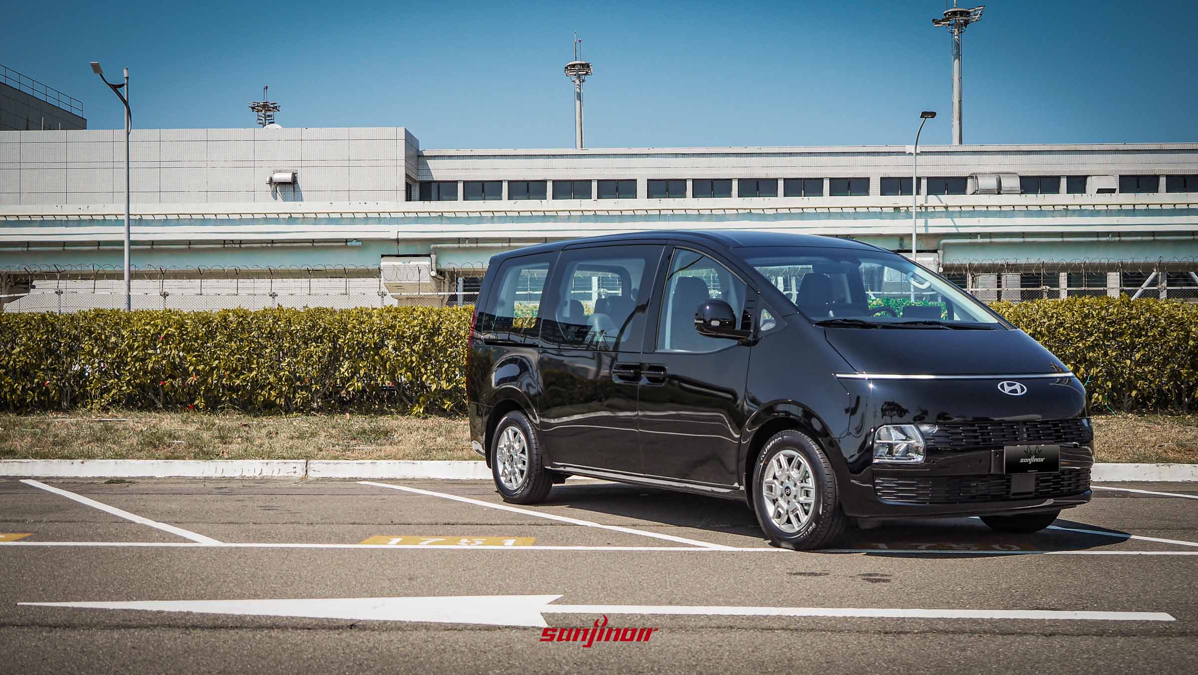 黑色 Hyundai Staria 停放於空曠停車場，展現出結合貫穿式日行燈與網格水箱護罩的星艦車頭設計。