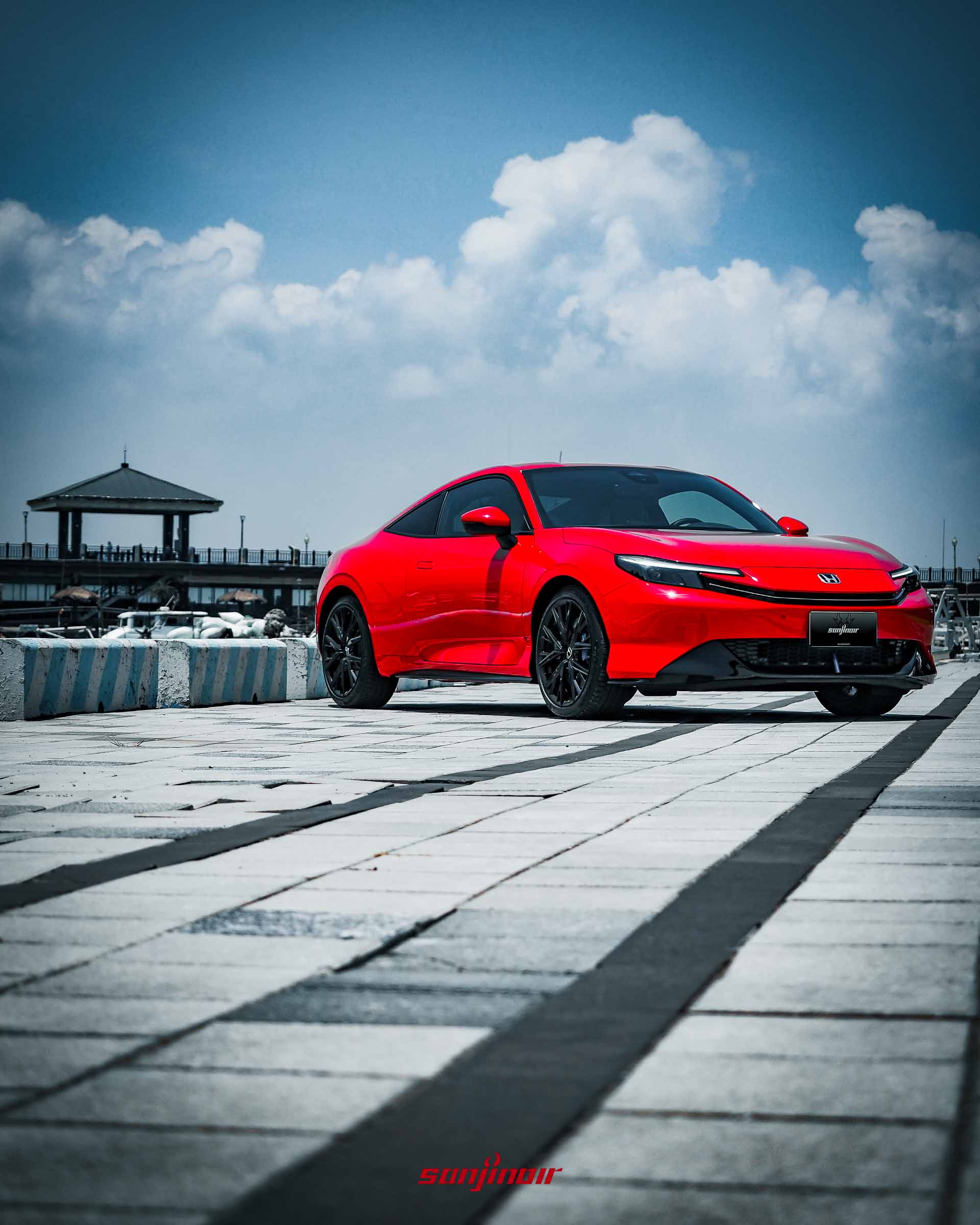 低角度拍攝的紅色HONDA Prelude前側視角,車身線條圓潤流暢,停放於晴朗的港灣邊。