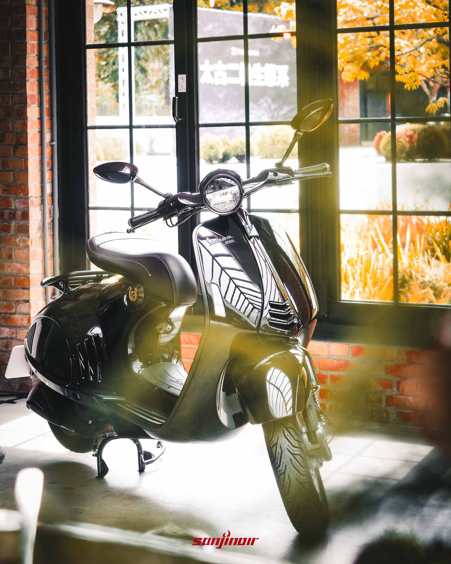 Vespa 946馬年特仕版摩托車的正面視角圖片，位於有紅磚牆和大型玻璃門的室內空間。全車身為全黑亮面配有單座墊，陽光透過玻璃門射入反射光線。背景玻璃門上方有模糊的太古二輪生態系字樣。