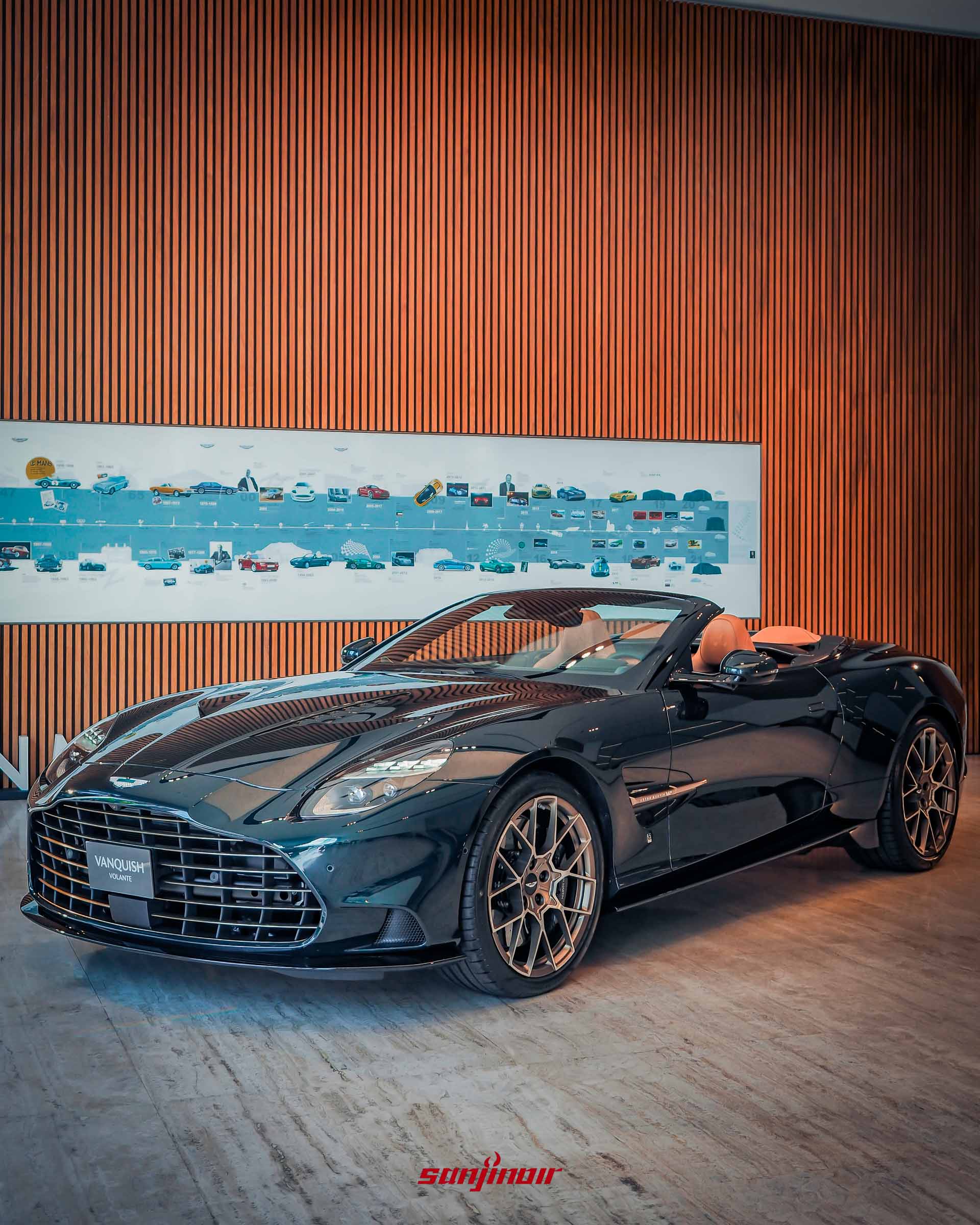 Pentland Green 深綠色 Aston Martin Vanquish Volante 60th Anniversary Edition 敞篷車的直角側視視角，軟頂收起。圖片展示其具侵略性的車側線條和 21 吋緞面古銅金輪圈。背景相同。