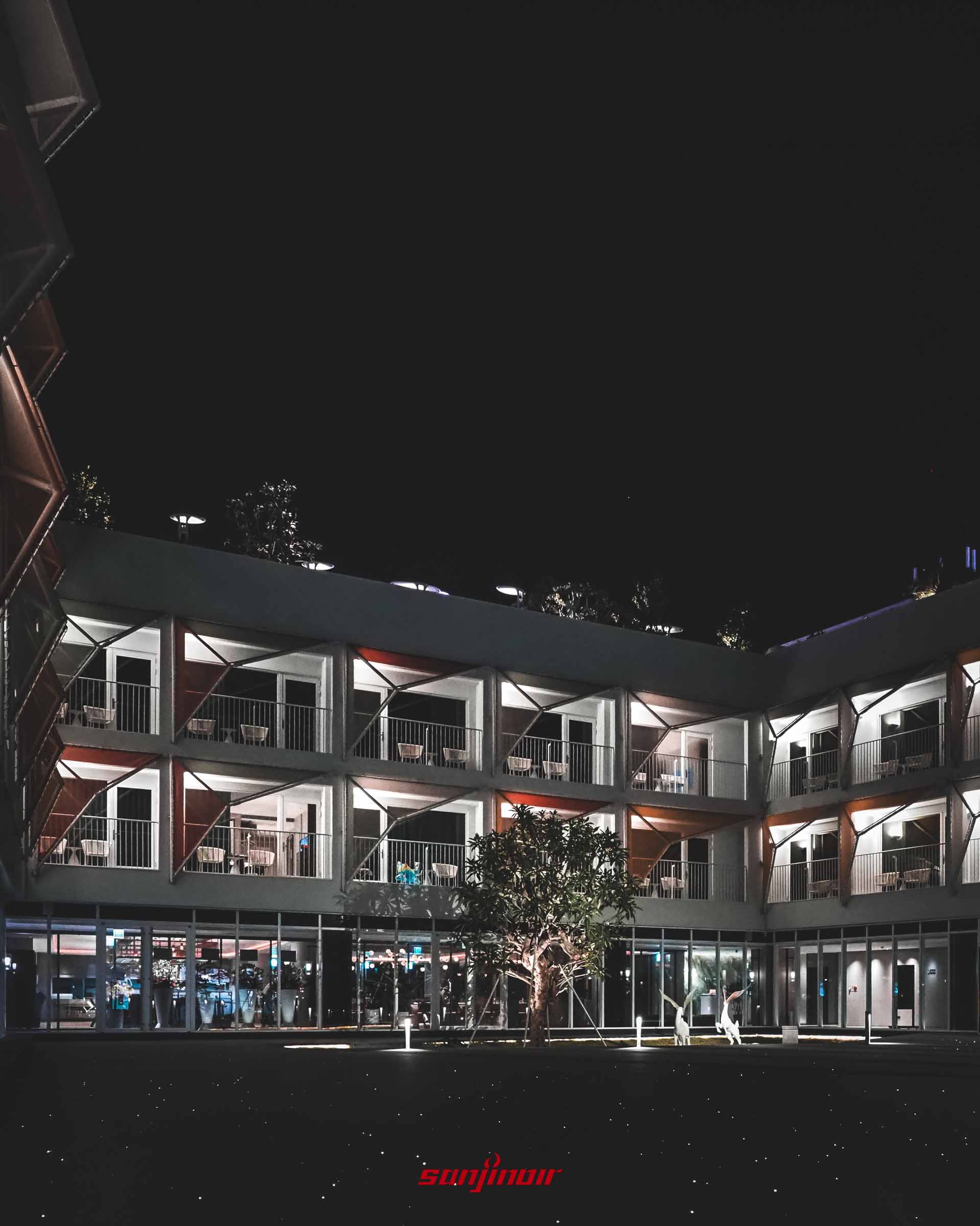 建築夜景外觀,白色客房環繞中庭,陽台設有彩色幾何遮陽板。