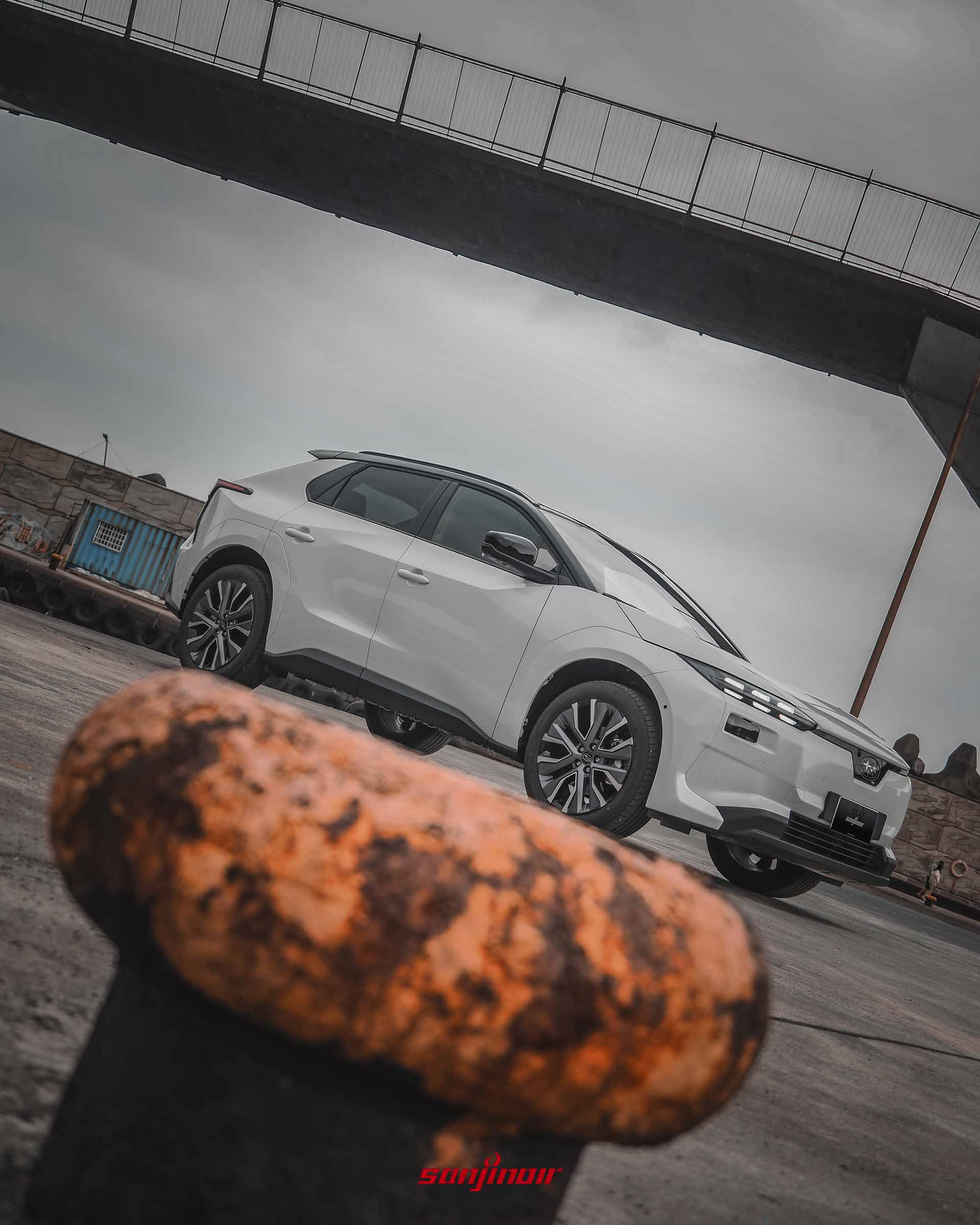由低角度拍攝的白色Subaru Solterra XT車頭側視圖，前景為生鏽的港邊繫船柱。