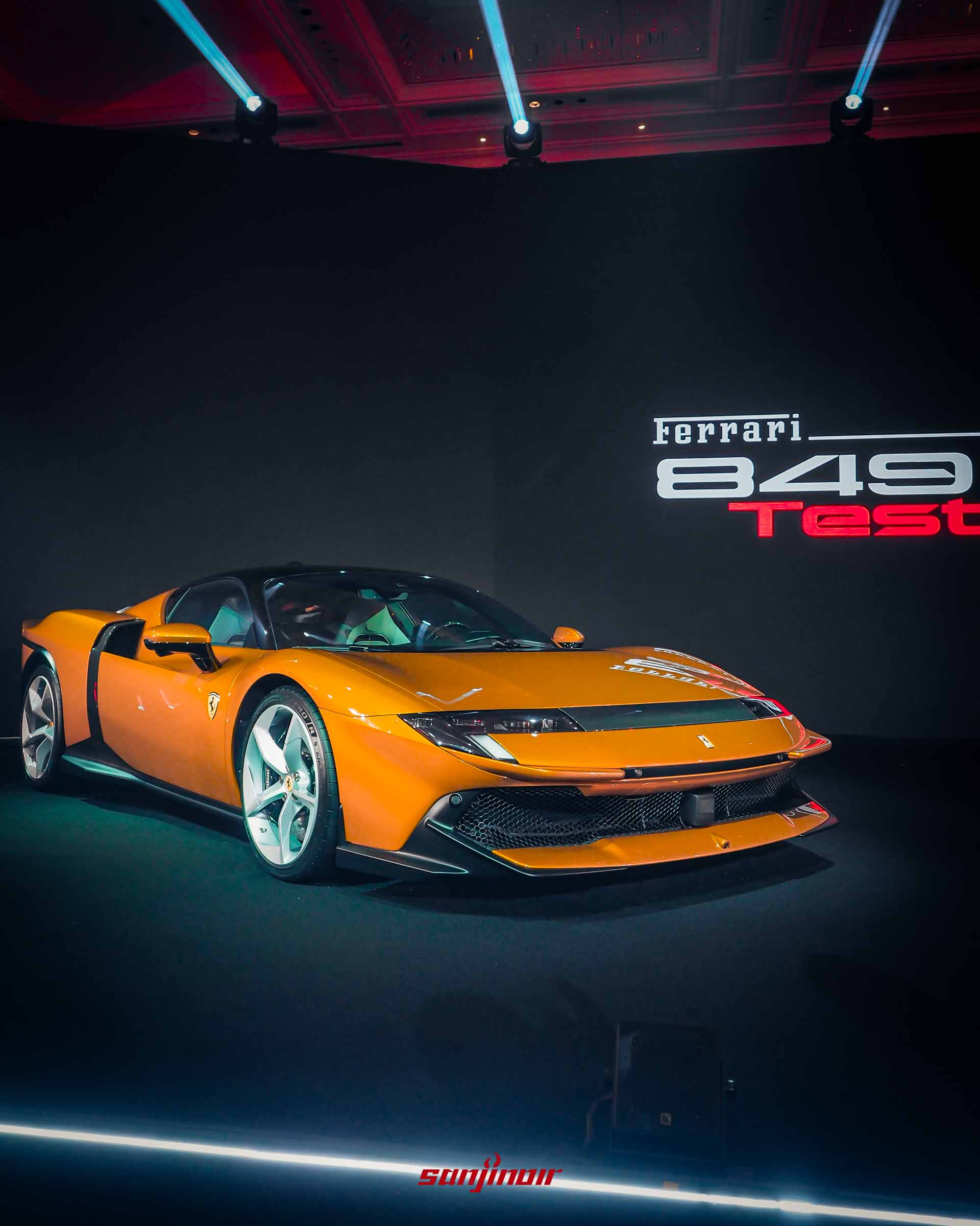 2026 Ferrari 849 Testarossa 橙色 Berlinetta 的前側 45 度視角，展現其從 1970 年代 Sports Prototype 汲取靈感的銳利幾何線條與立體輪廓。舞台燈光 (藍、紅、白) 聚焦在車款上。