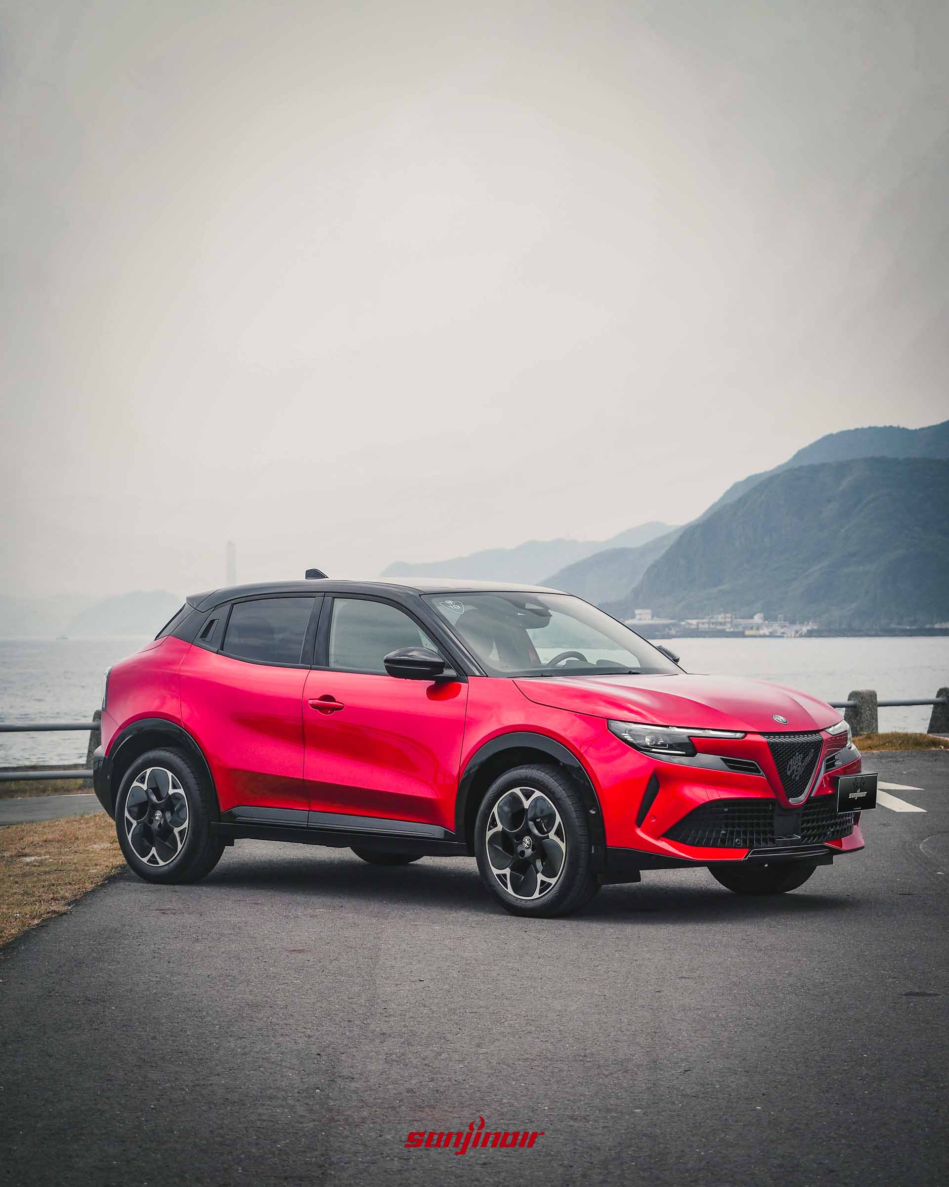 紅色Alfa Romeo Junior停在海邊道路,車側呈現緊湊的B-SUV比例與黑色輪拱。
