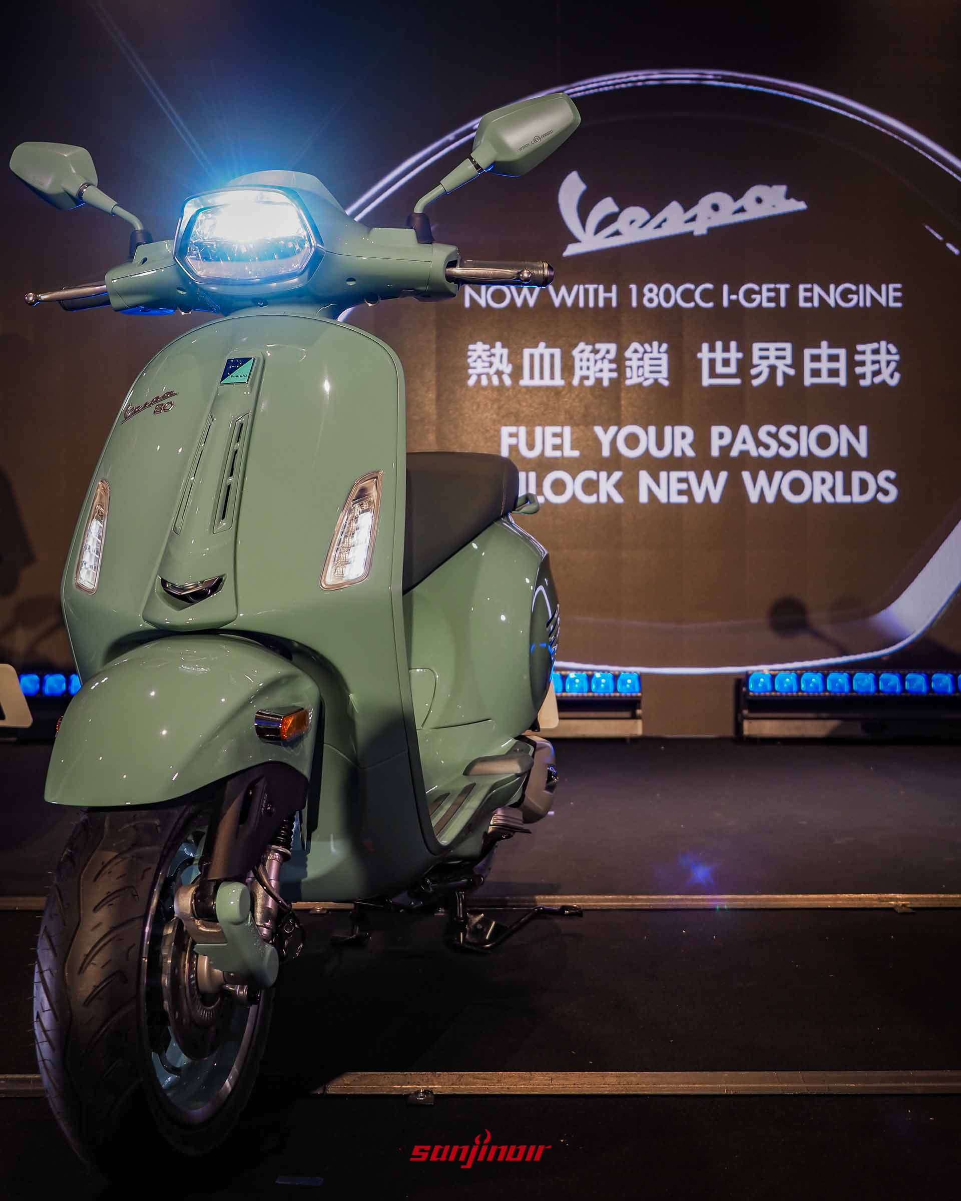 發表會現場,一台經典粉彩綠的 Vespa Sprint 80th 特仕版速克達,車燈亮起,從斜前方近距離拍攝。