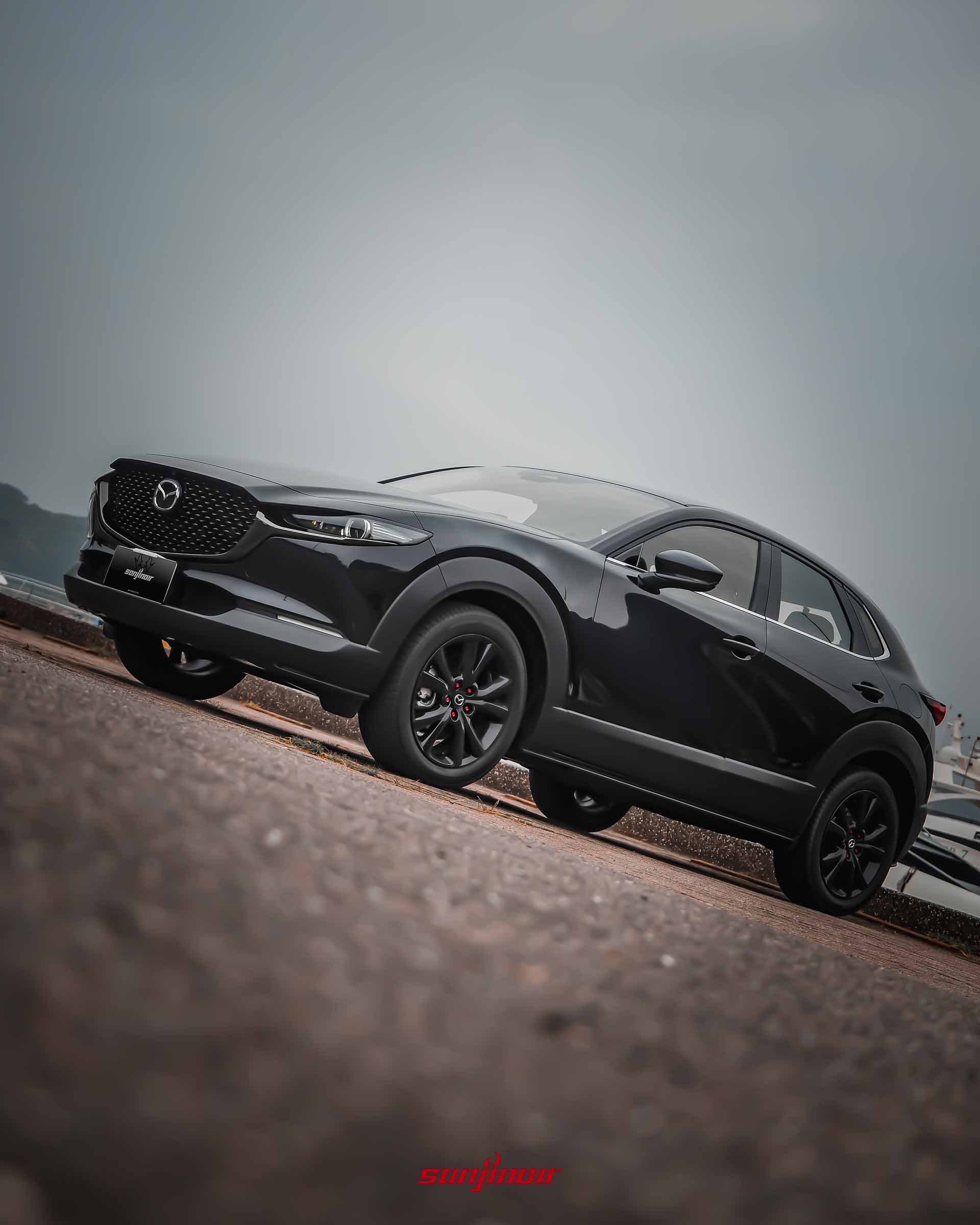 低角度拍攝黑色MAZDA CX-30 20S Homura車頭側視圖,突顯其曜黑水箱護罩與流線車身設計。