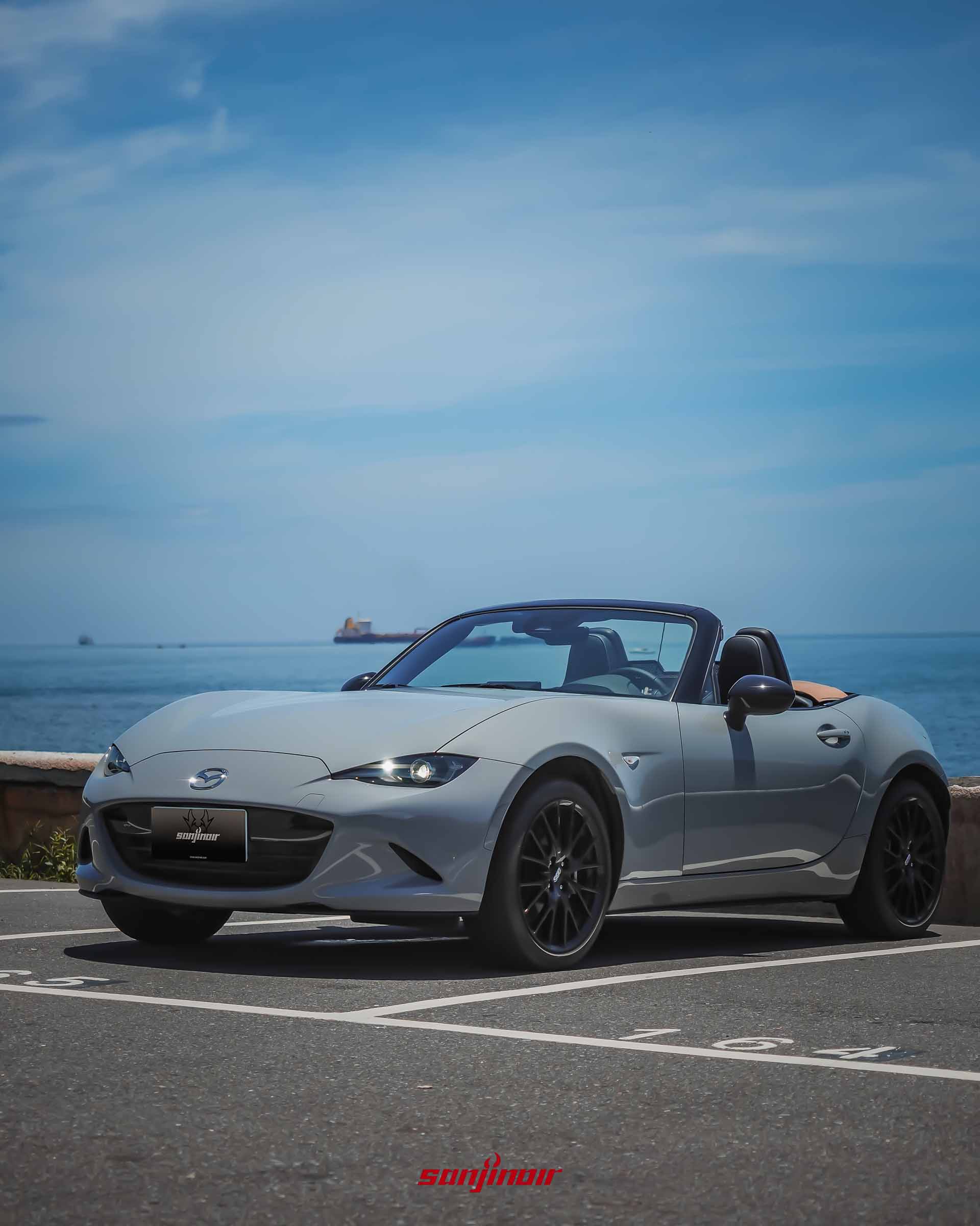 灰色MAZDA MX-5 RS開篷狀態右前側45度視角,停放於海邊,背景可見海平面與船隻。