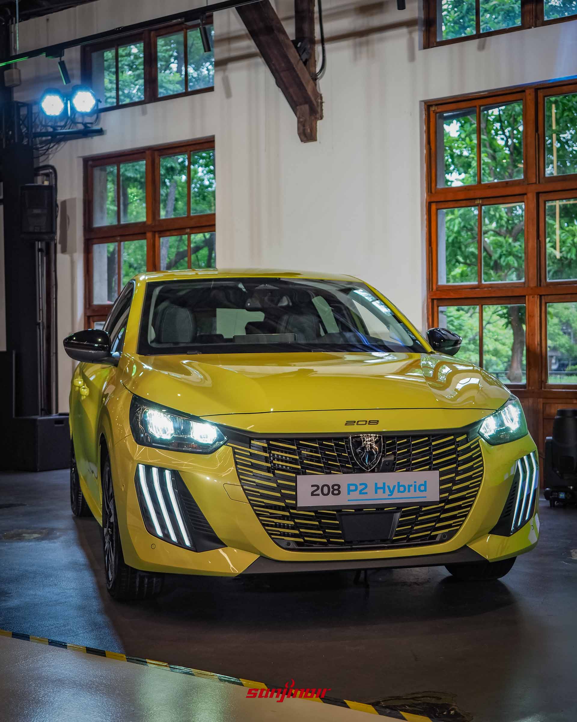 鮮黃色PEUGEOT 208 P2 Hybrid的車頭正面特寫,大燈與三爪式LED日行燈點亮,正中央為全新PEUGEOT盾形廠徽與208字樣。