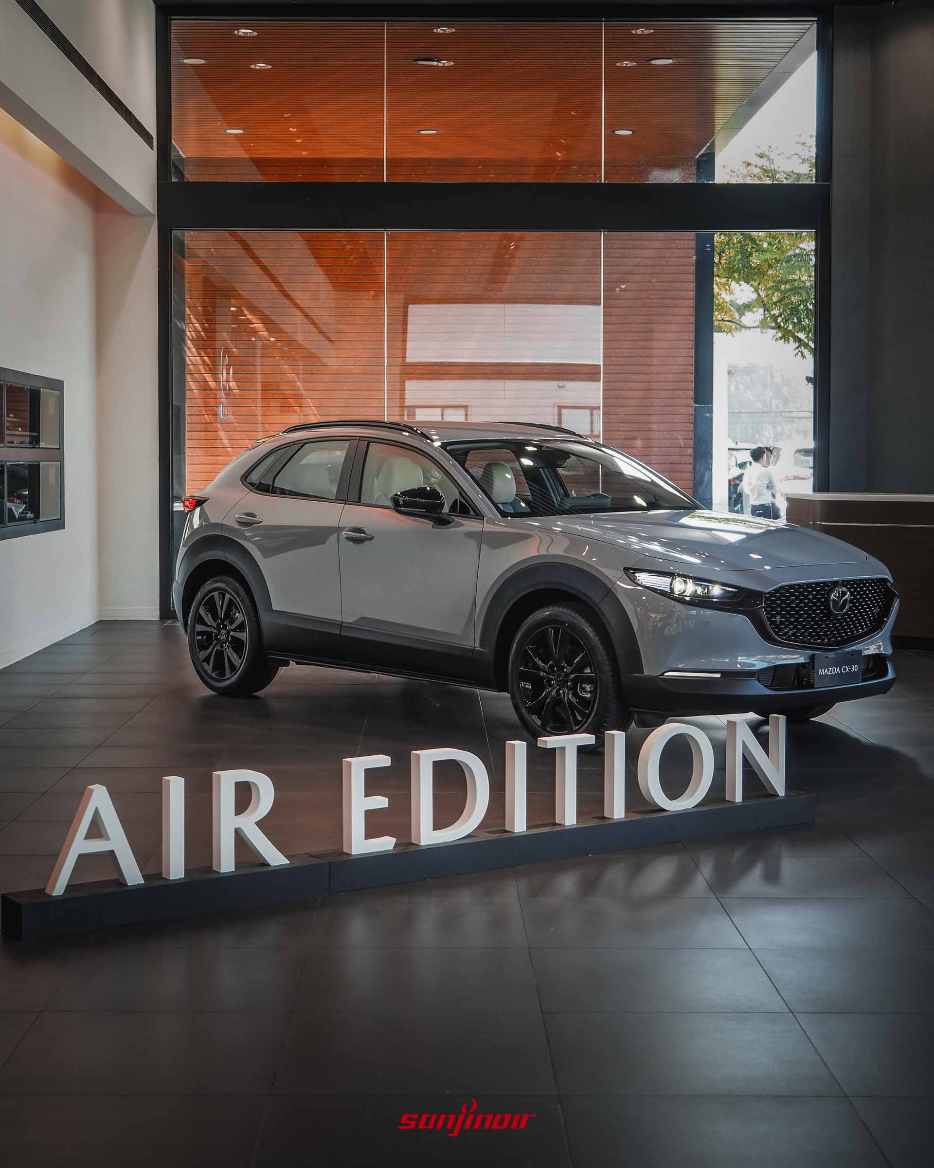 展間內的MAZDA CX-30 Air Edition全車側前視圖,展示天際灰車色與黑化套件的對比,前方有AIR EDITION裝飾字樣。