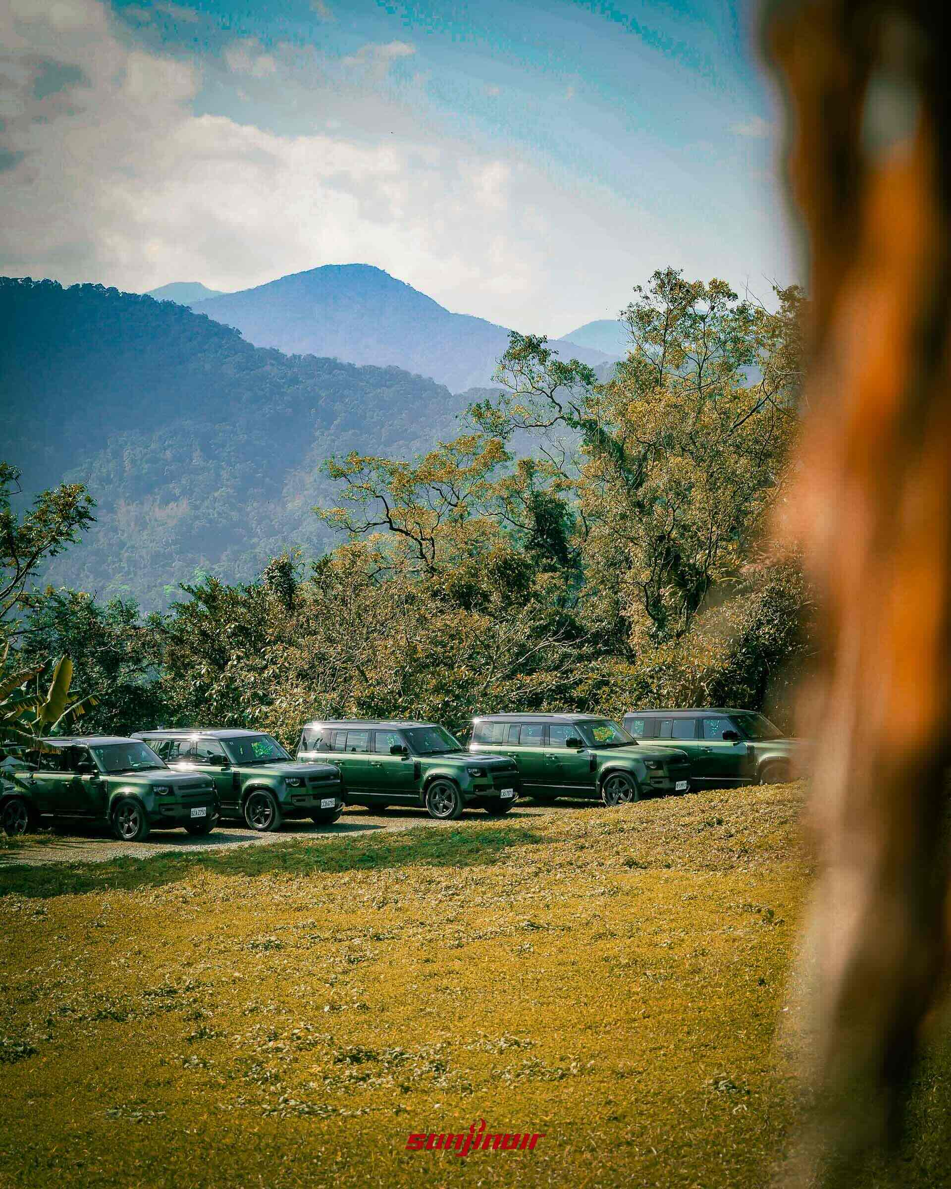 多輛綠色Defender整齊停放於草地上後方為層疊山巒。