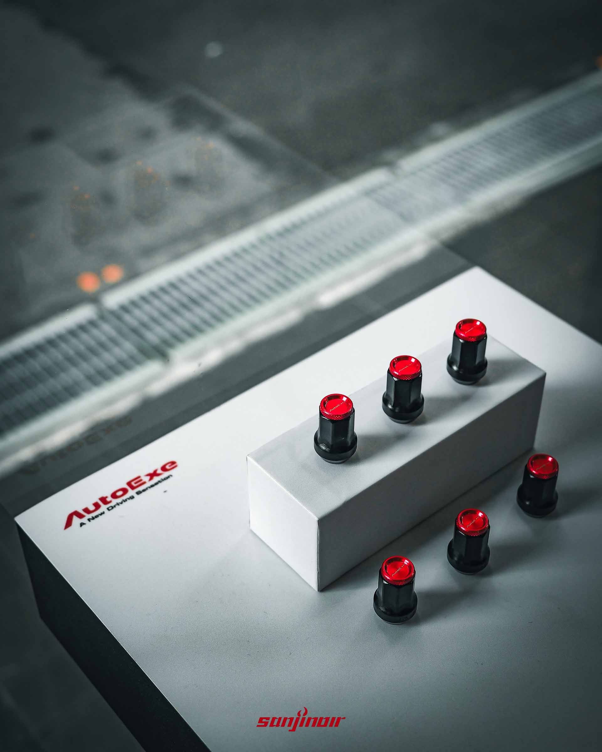 AutoExe 品牌展示台上的湛紅高剛性防盜螺帽特寫，採用黑紅雙色設計與七角形防盜造型。