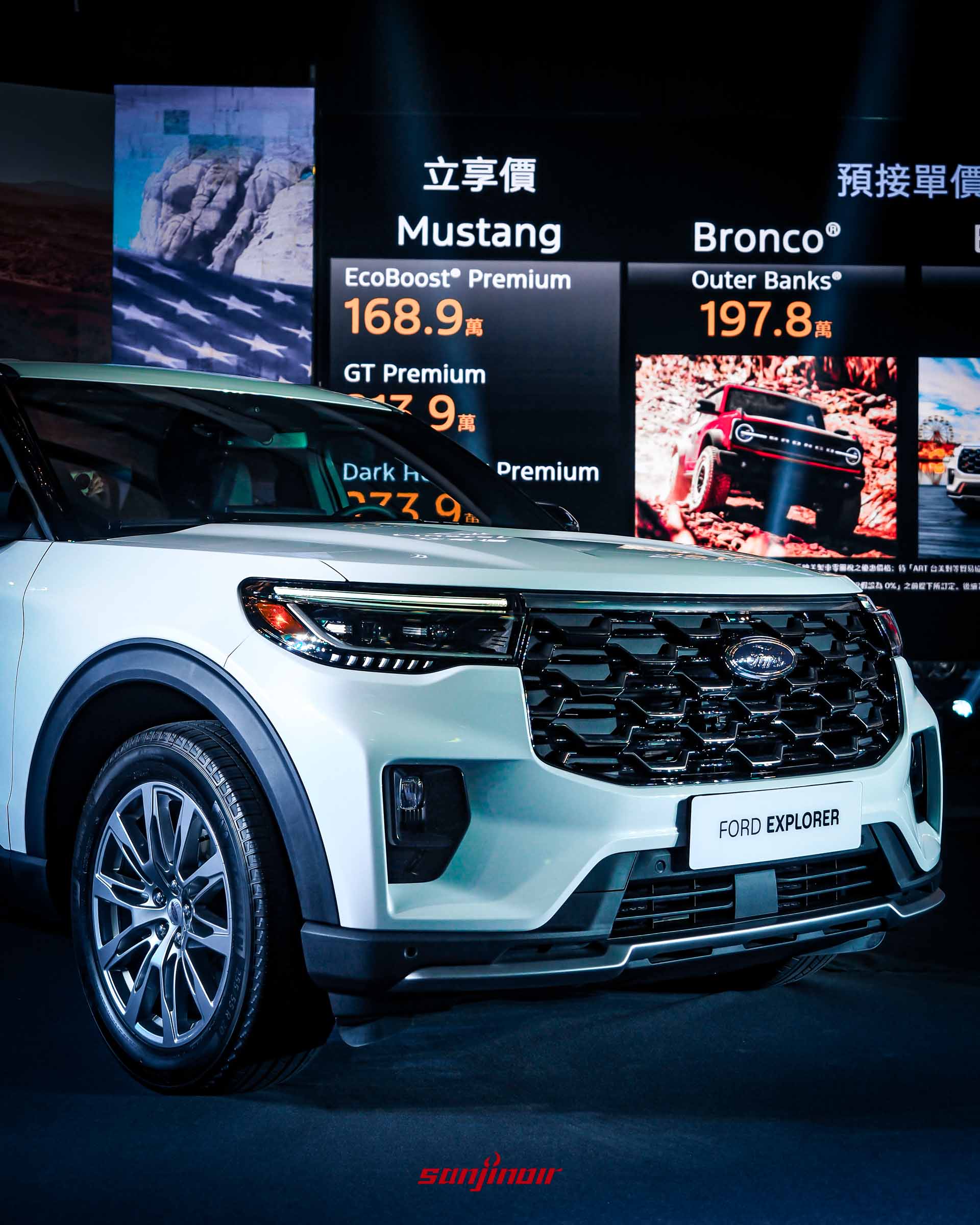 發表會現場近景。白色Ford Explorer的前臉位於前景，車牌顯示「FORD EXPLORER」。背景大螢幕顯示「立享價 Mustang」和「預接單價 Bronco® Outer Banks® TWD 1,978,000」字樣，以及一輛紅色Bronco衝刺的圖片。