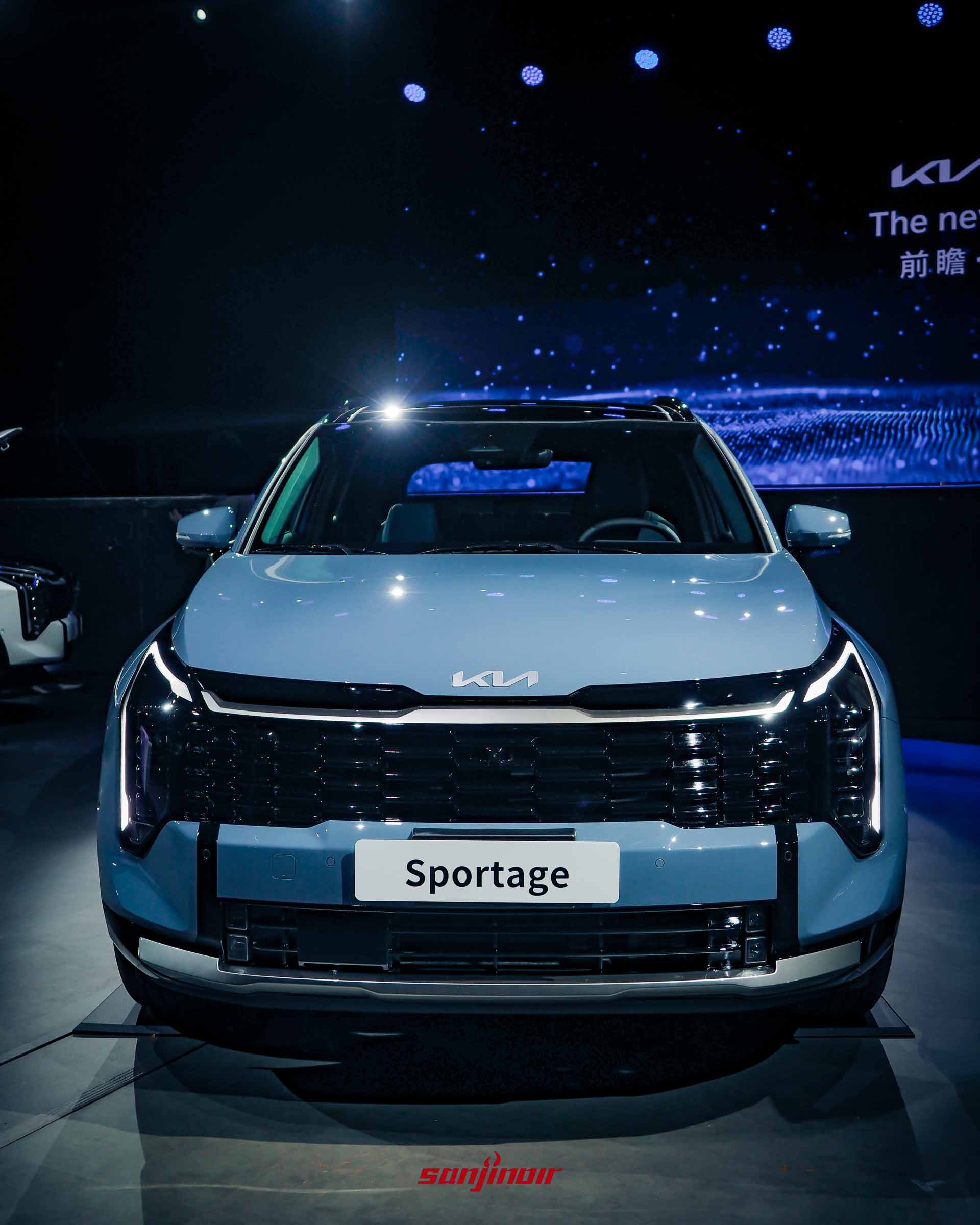 一台晨霧藍Kia Sportage的正前方視角，展示垂直排列的LED頭燈和日行燈、大面積網格水箱護罩、全新KIA LOGO以及車牌上的Sportage字樣。