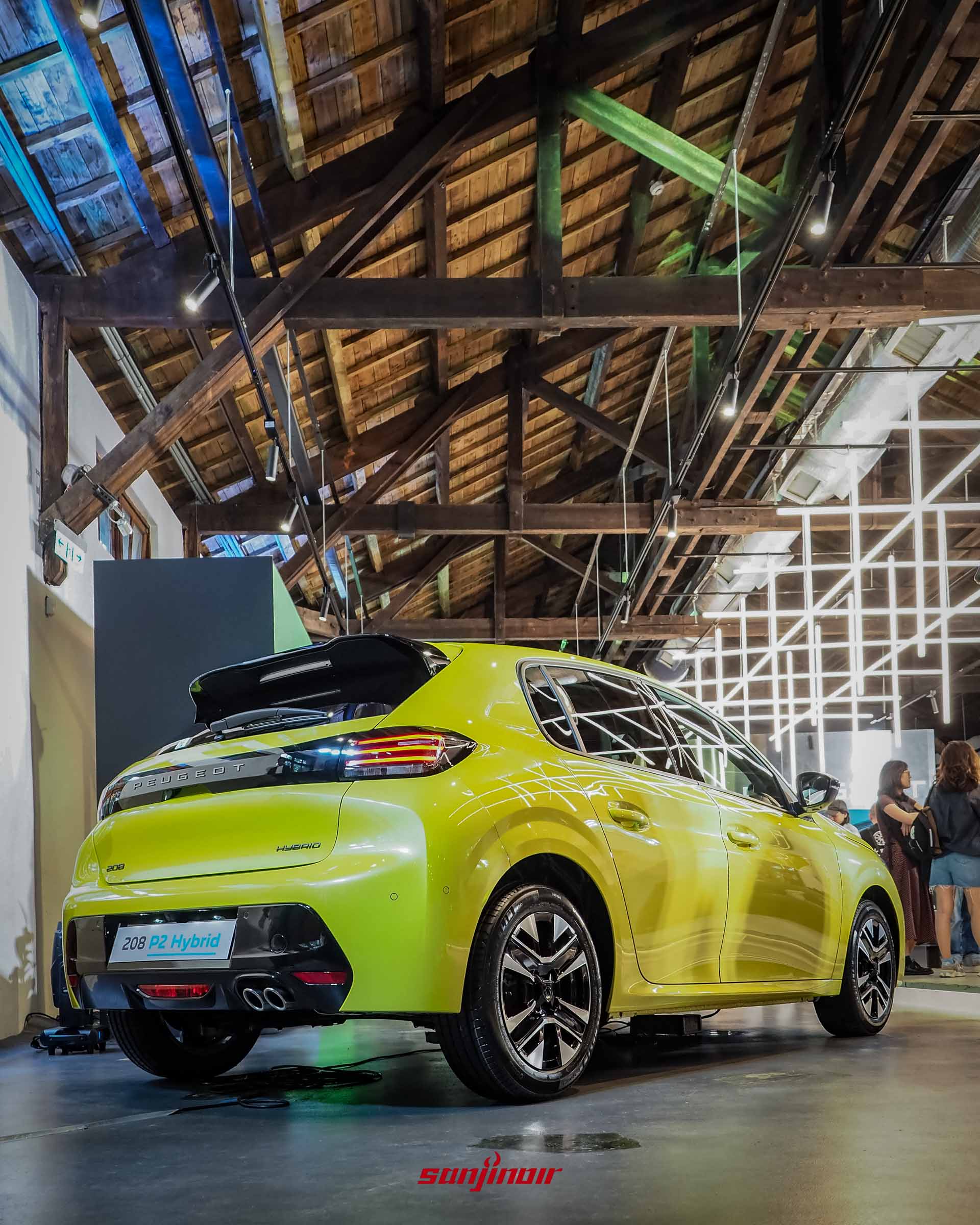 自左後方拍攝的黃色PEUGEOT 208 P2 Hybrid,展示亮黑色的車頂擾流板、橫向LED尾燈組以及底部的雙出排氣尾管配置。