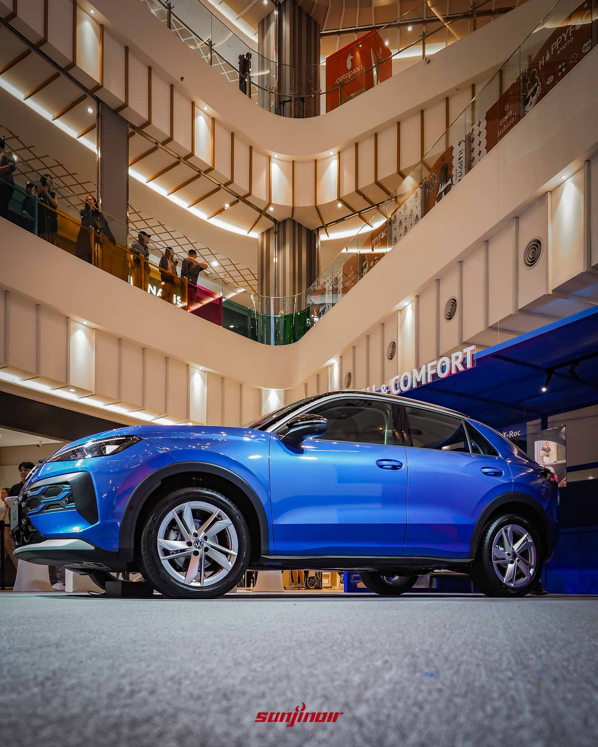 藍色 Volkswagen T-Roc 於多層樓商場展區的側面全車照,展示其斜背車頂輪廓、雙色車身設計與鋁合金輪圈。