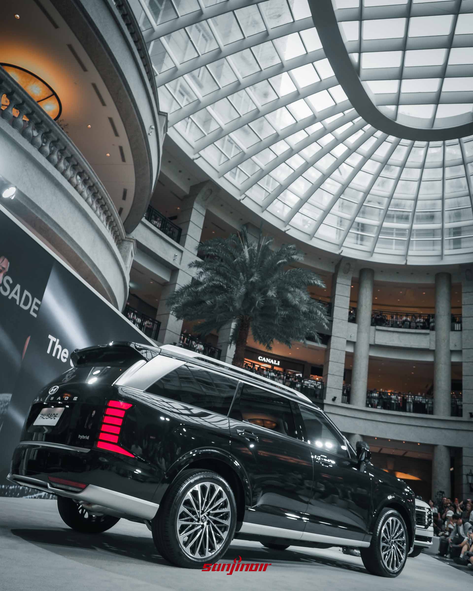 2026 Hyundai Palisade黑色車型左後方外觀，展示紅色直列式LED尾燈與鋁圈，背景為挑高採光罩的百貨商場內部。