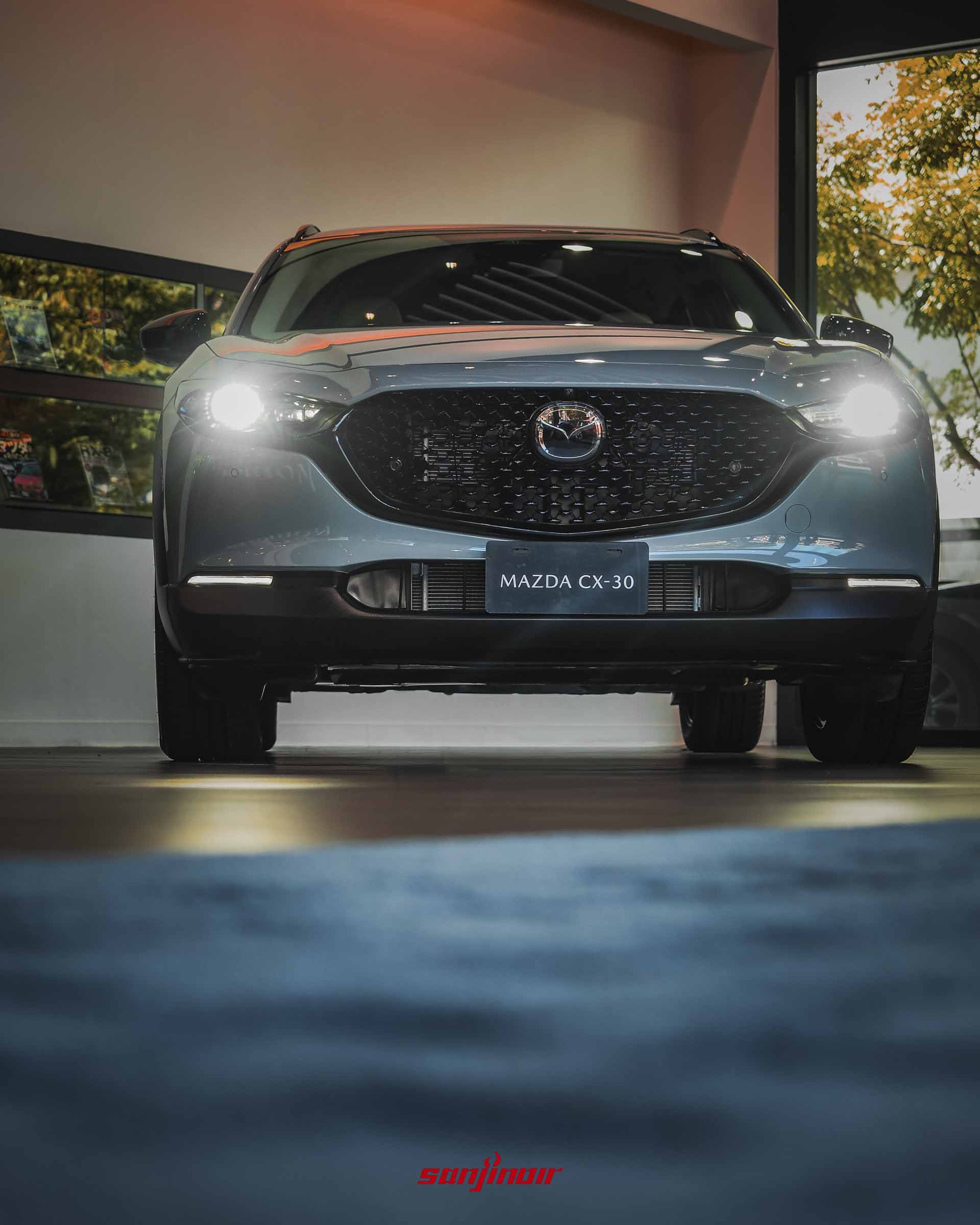 低角度拍攝的MAZDA CX-30 Air Edition車頭正面照,頭燈點亮,特寫黑化網狀水箱護罩與黑鉻廠徽。