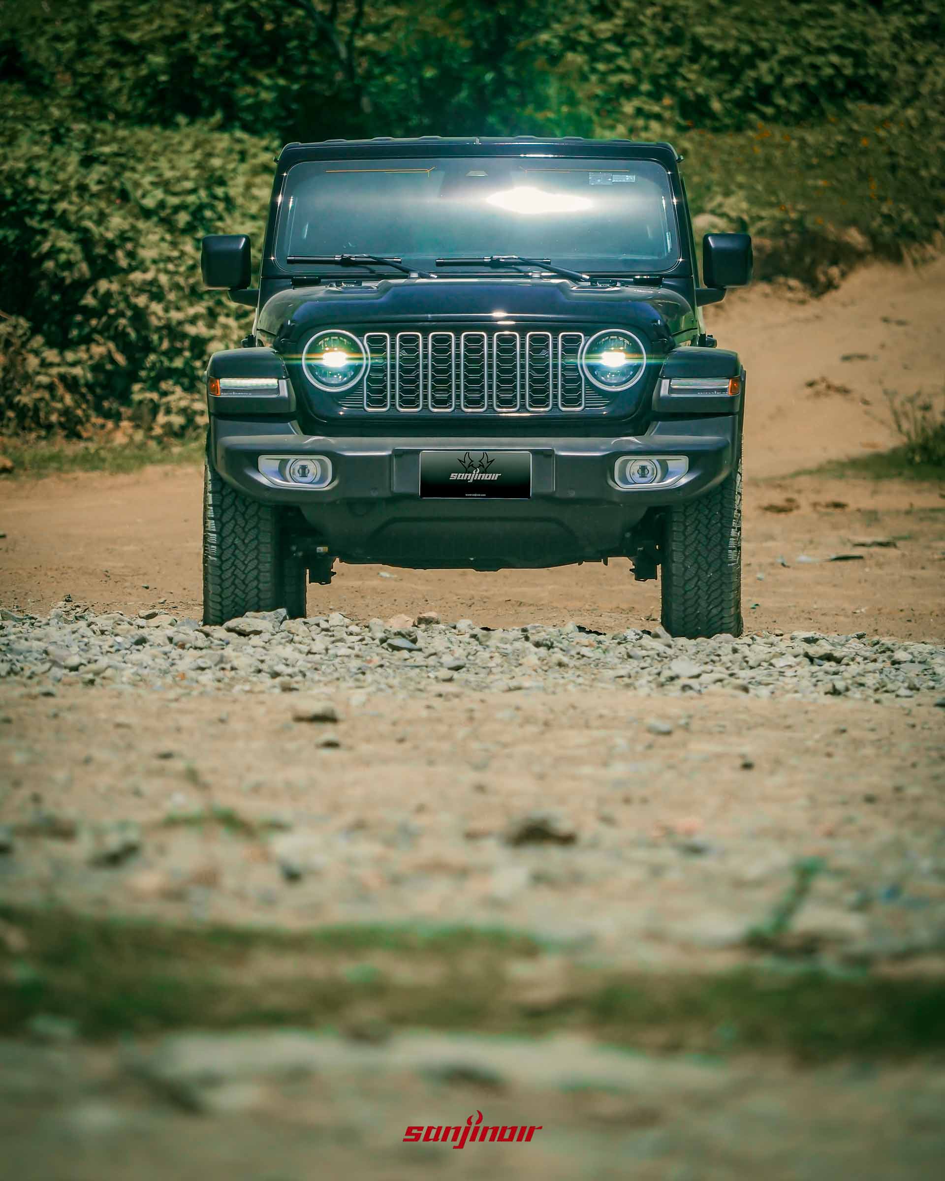 Jeep Wrangler Sahara 的車頭特寫,圓形大燈亮起,背景為模糊的沙地。