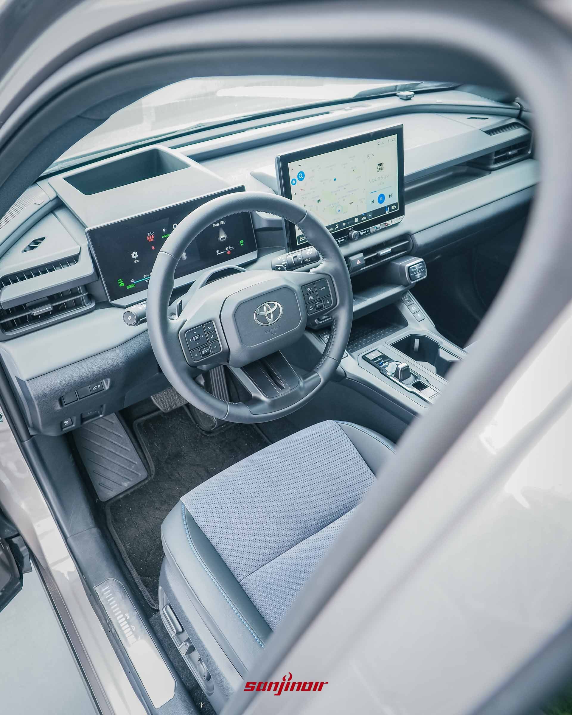 從駕駛座車門外望向RAV4 PHEV車室內裝,包含方向盤、雙螢幕配置及中央鞍座設計。
