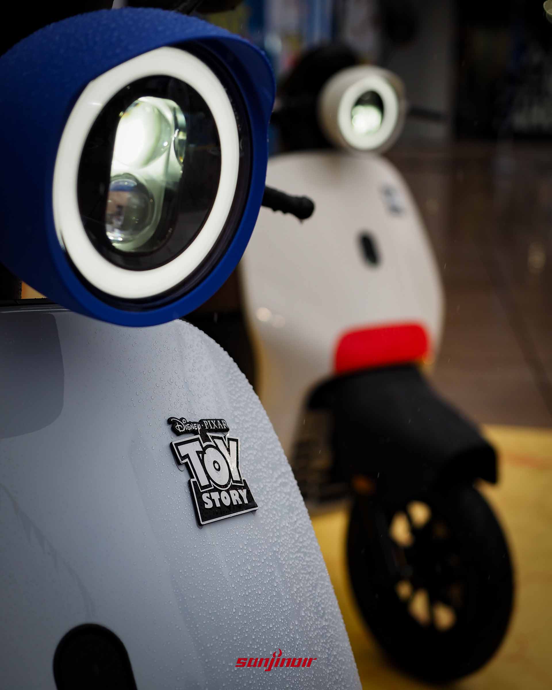 Gogoro EZZY 500機車車頭特寫，顯示玩具總動員金屬徽章與藍色矽膠頭燈套，表面佈滿水滴。