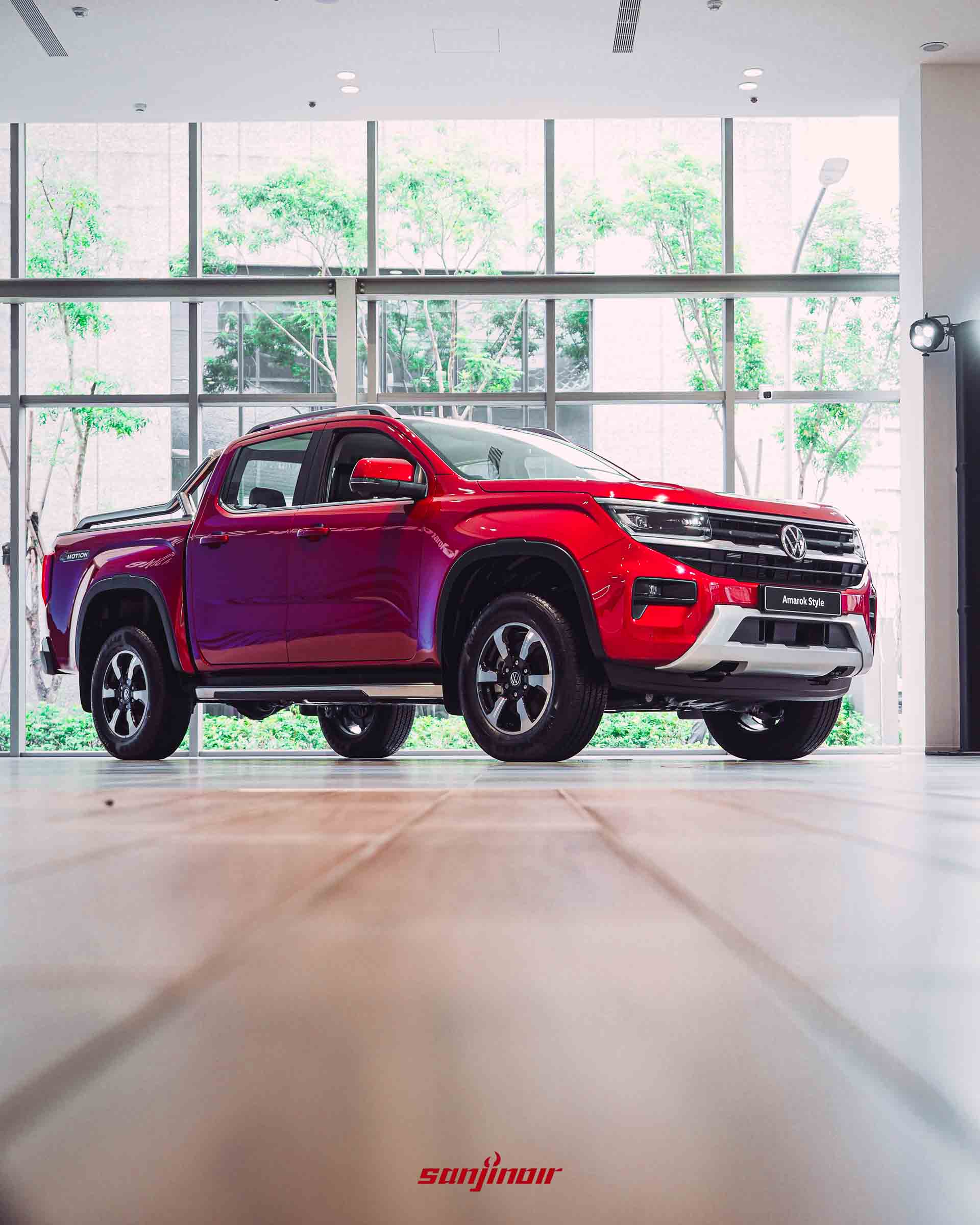 低角度拍攝的紅色Volkswagen Amarok Style側面，展示車身線條、18吋輪圈與車頂架，背景為大片落地窗。