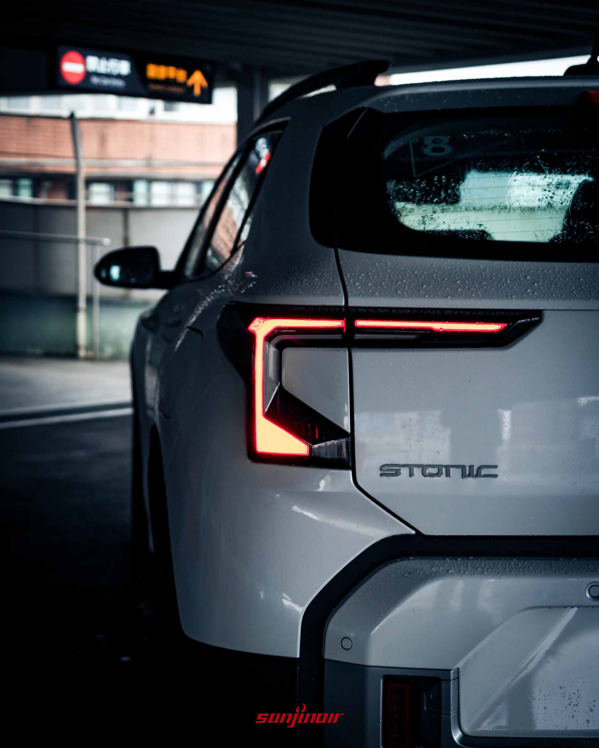 白色2026 Kia Stonic左後車尾燈的近距離特寫,雨滴附著於車身上,展示幾何折線設計的LED尾燈與下方Stonic銘牌。