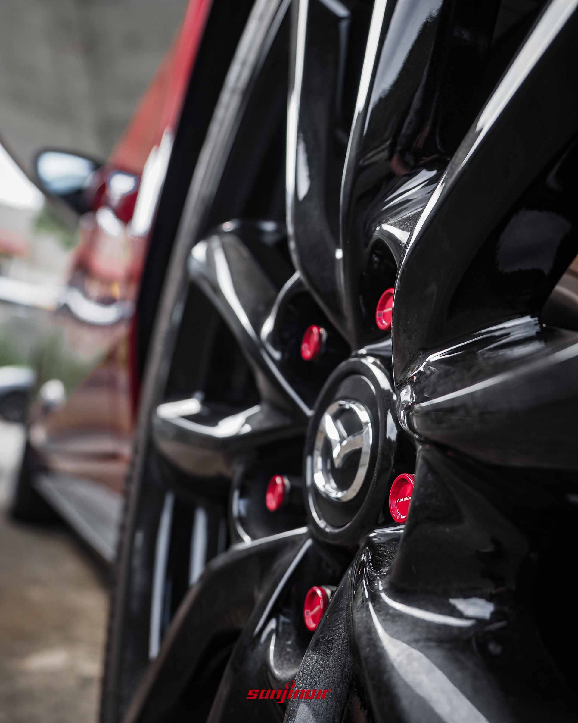 黑色的爍黑鋁合金輪圈，中央有MAZDA標誌，安裝了鮮豔紅色的AutoExe湛紅高剛性防盜螺帽。