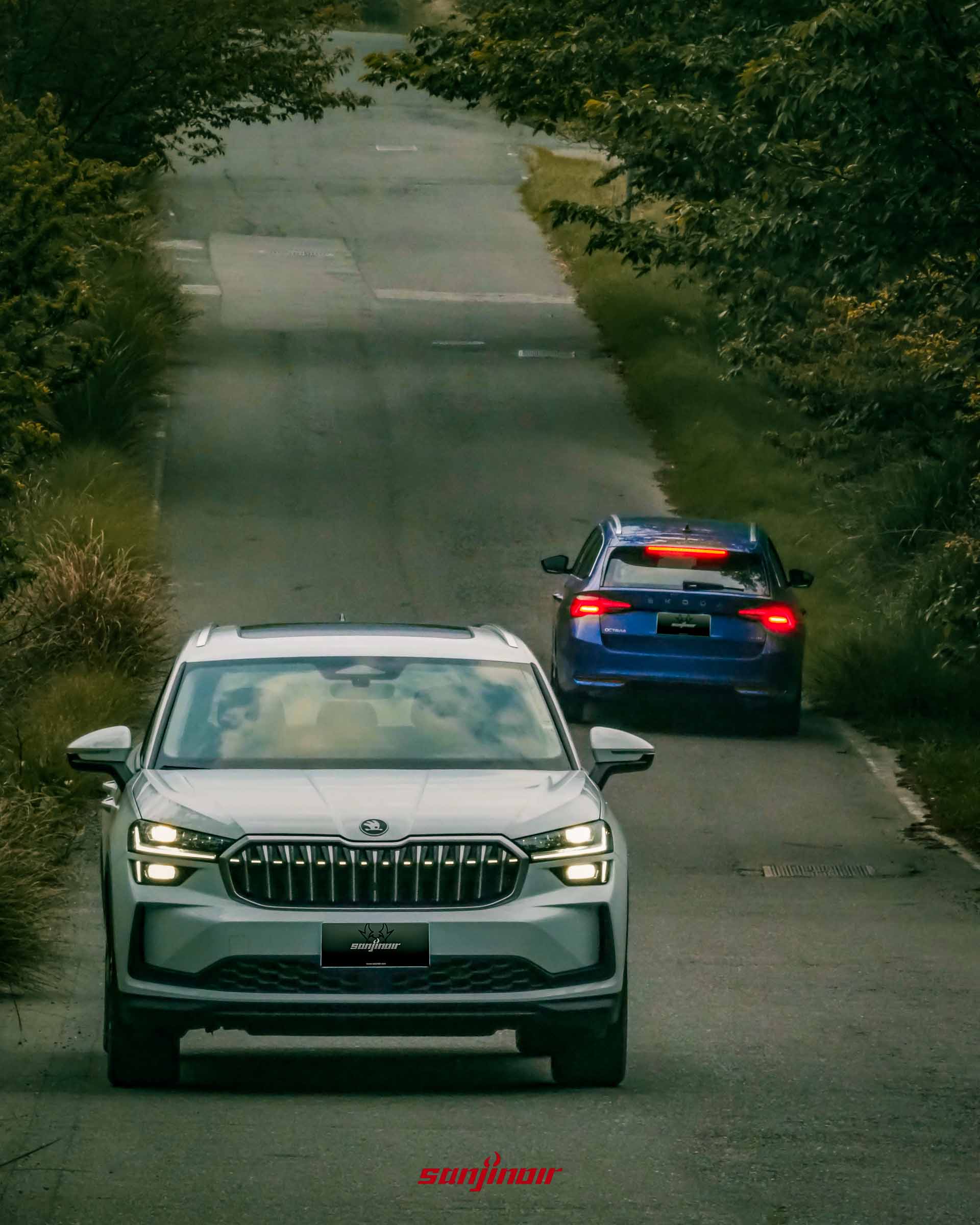 白色 Škoda Kodiaq 2.0 TSI 4×4 車頭朝向鏡頭行駛，後方遠處有藍色 Octavia Combi 2.0 TSI 4×4 駛離鏡頭的背影，行駛於山區道路。
