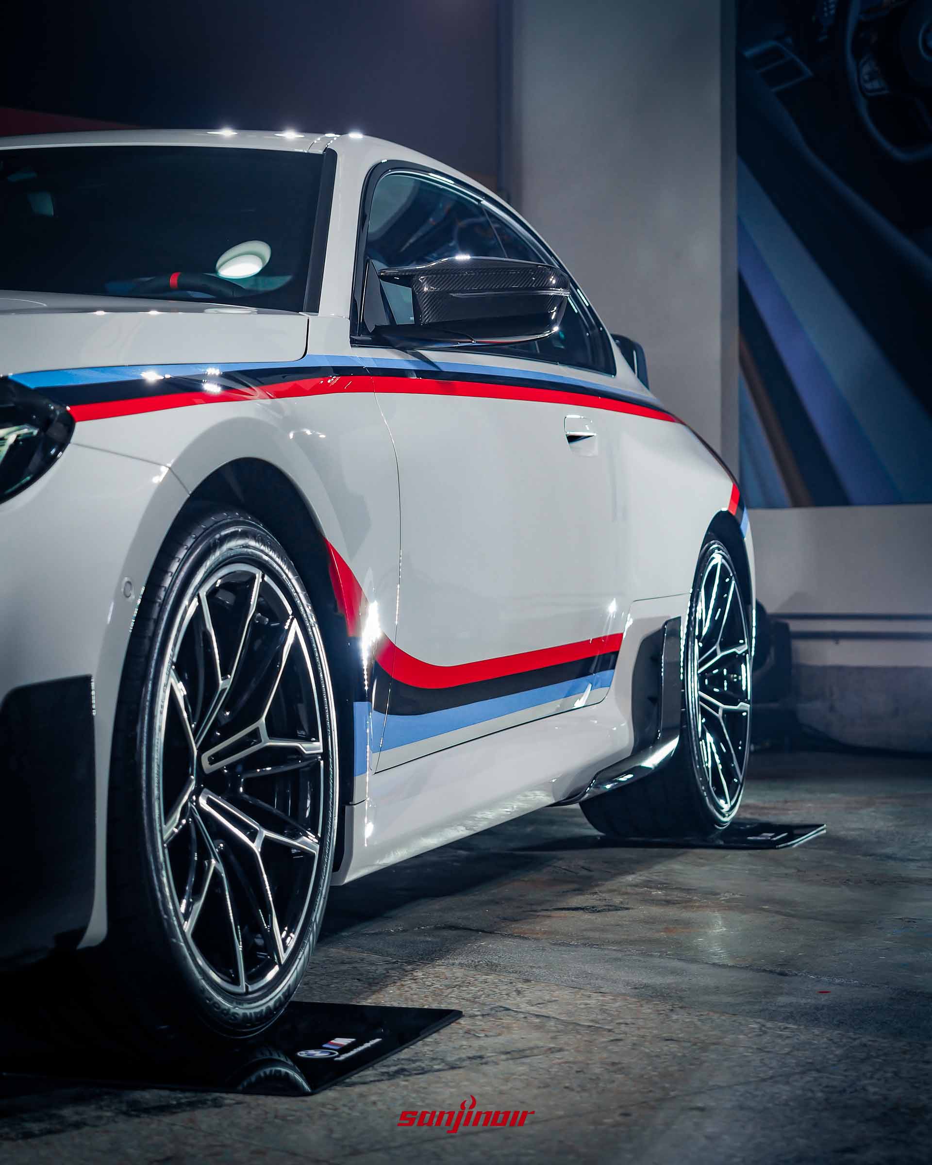 白色BMW M2車側特寫照，展示前輪圈造型以及車門下半部的M三色手工烤漆線條與碳纖維側裙飾板。