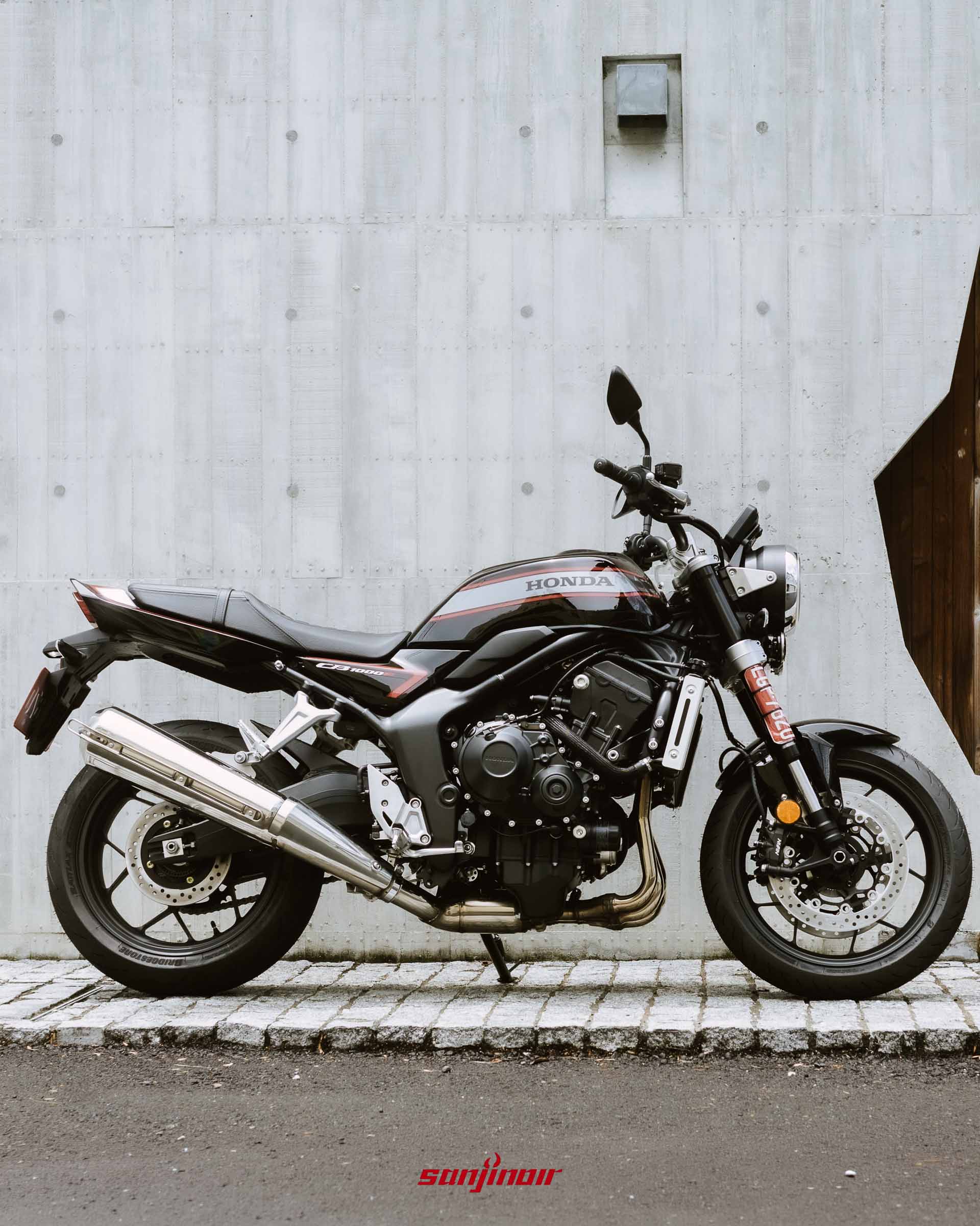 黑色Honda CB1000F停放於石板路上的車身右側全景照片,背景為清水模牆面。