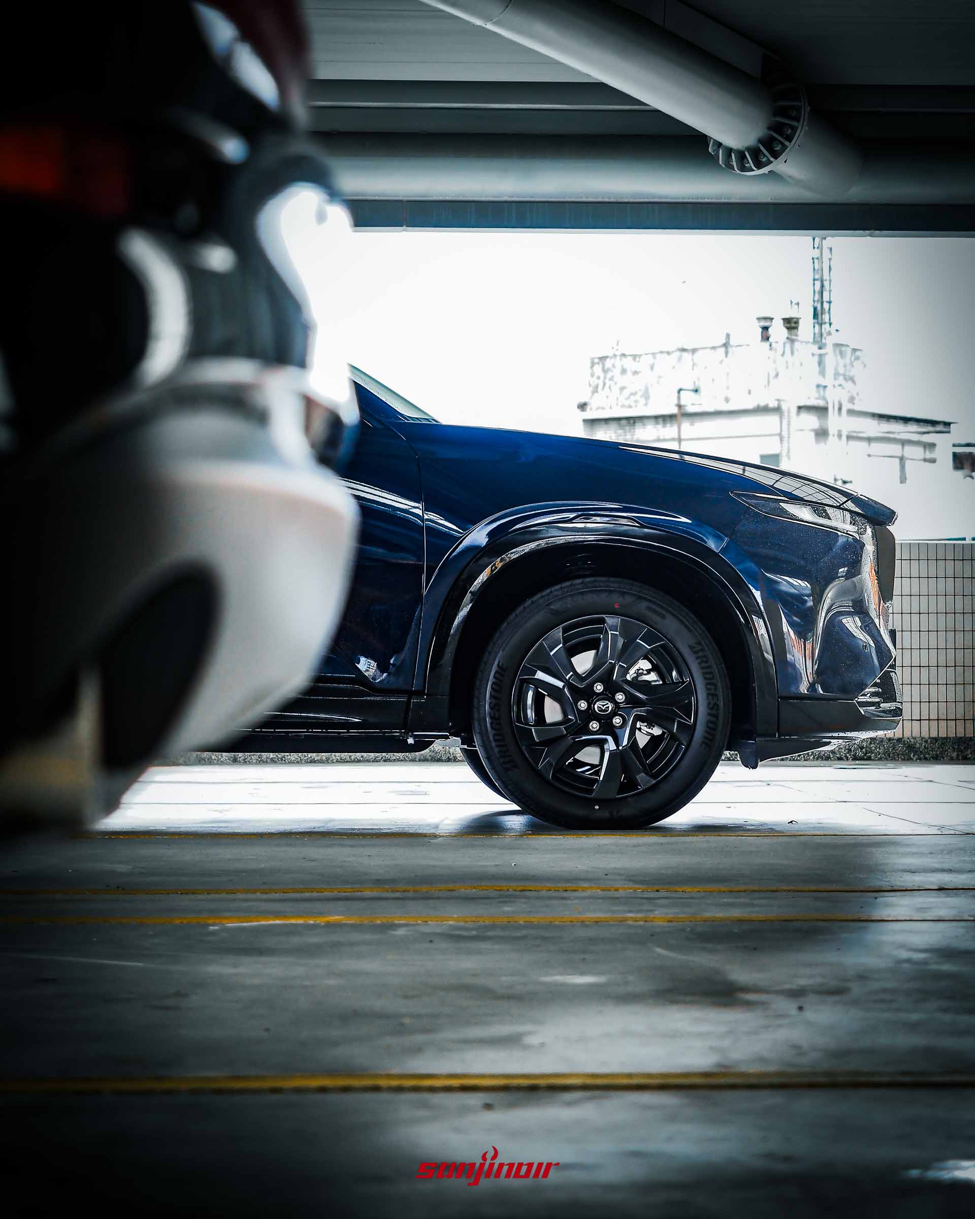 從車尾排氣管視角望向MAZDA CX-5前輪19吋黑色切削輪圈的低角度特寫。