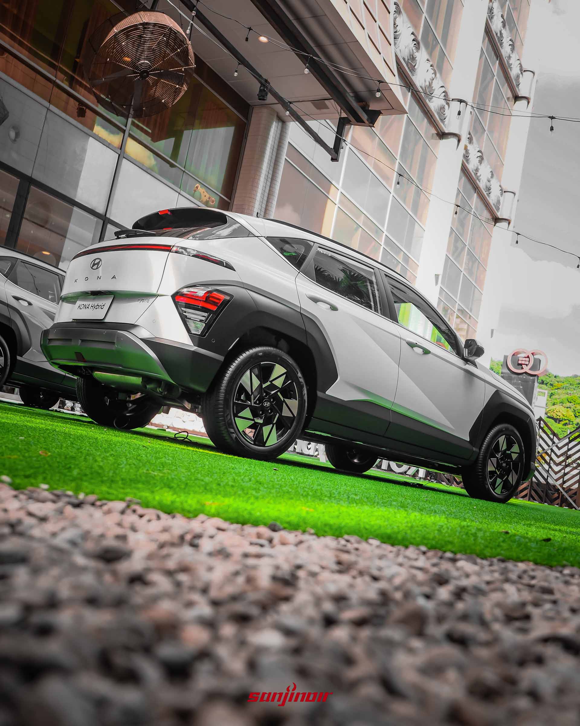 從碎石地面的極低角度往上仰拍Kona Hybrid的左後車側。展示了貫穿式LED尾燈組、車尾銘牌、18吋雙色鋁圈,以及車側明顯的Z-Shape立體折線。