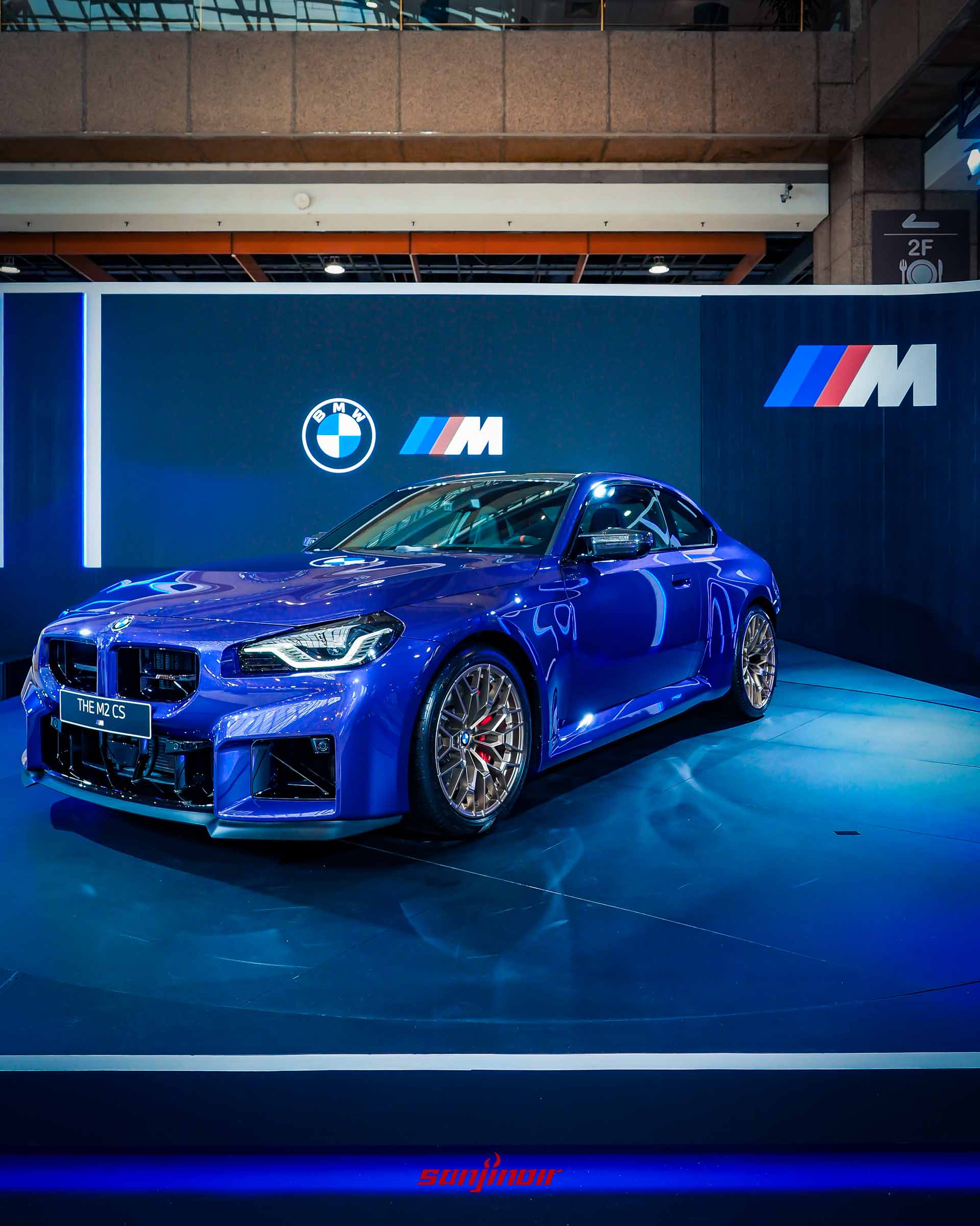 藍色BMW M2 CS性能跑車於BMW M Power展區舞台上，背景有巨大的M標誌。