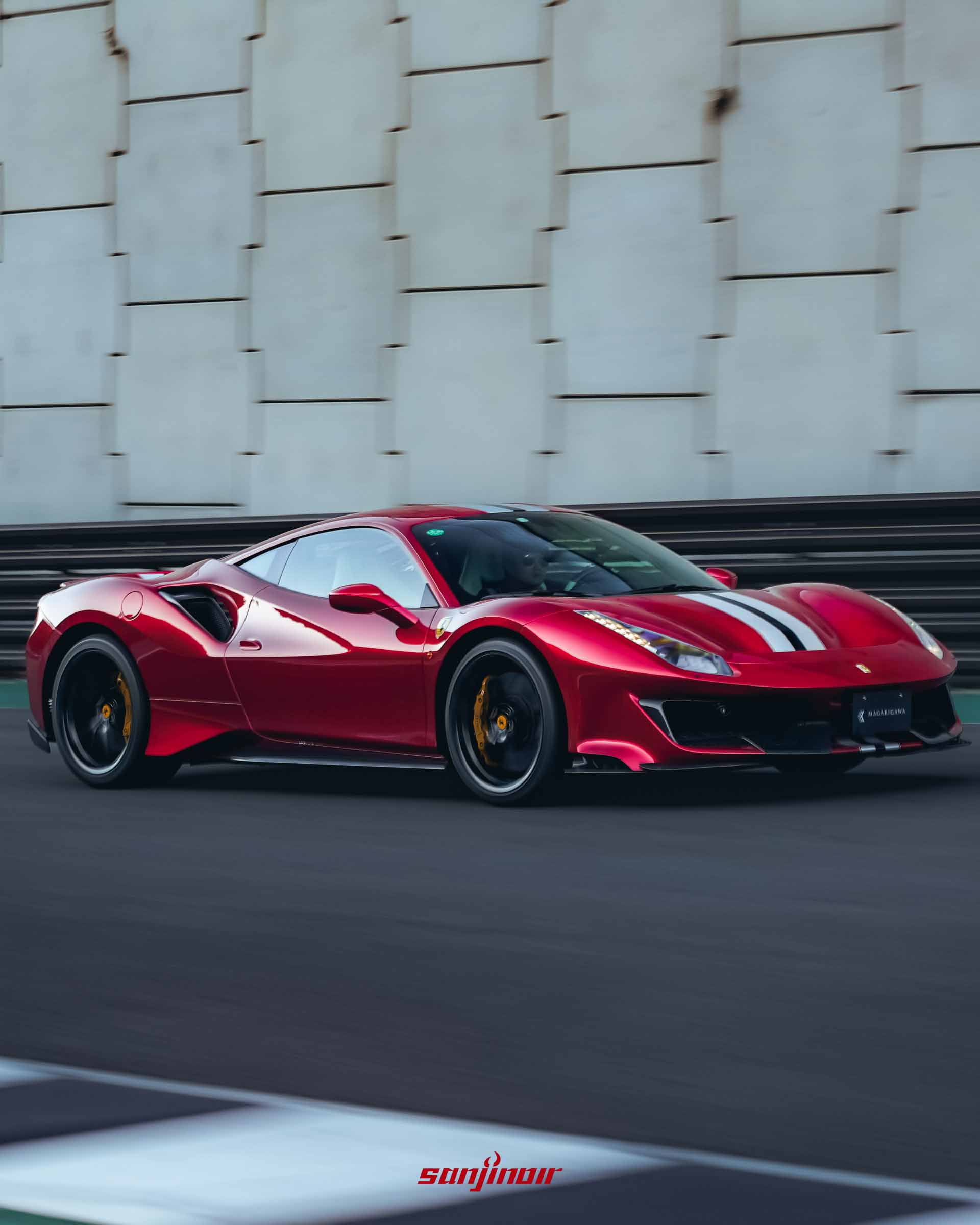 處於動態行駛中的紅色 Ferrari 488 Pista 側面特寫，車輪呈現高速旋轉的模糊感，背景為水泥擋土牆。