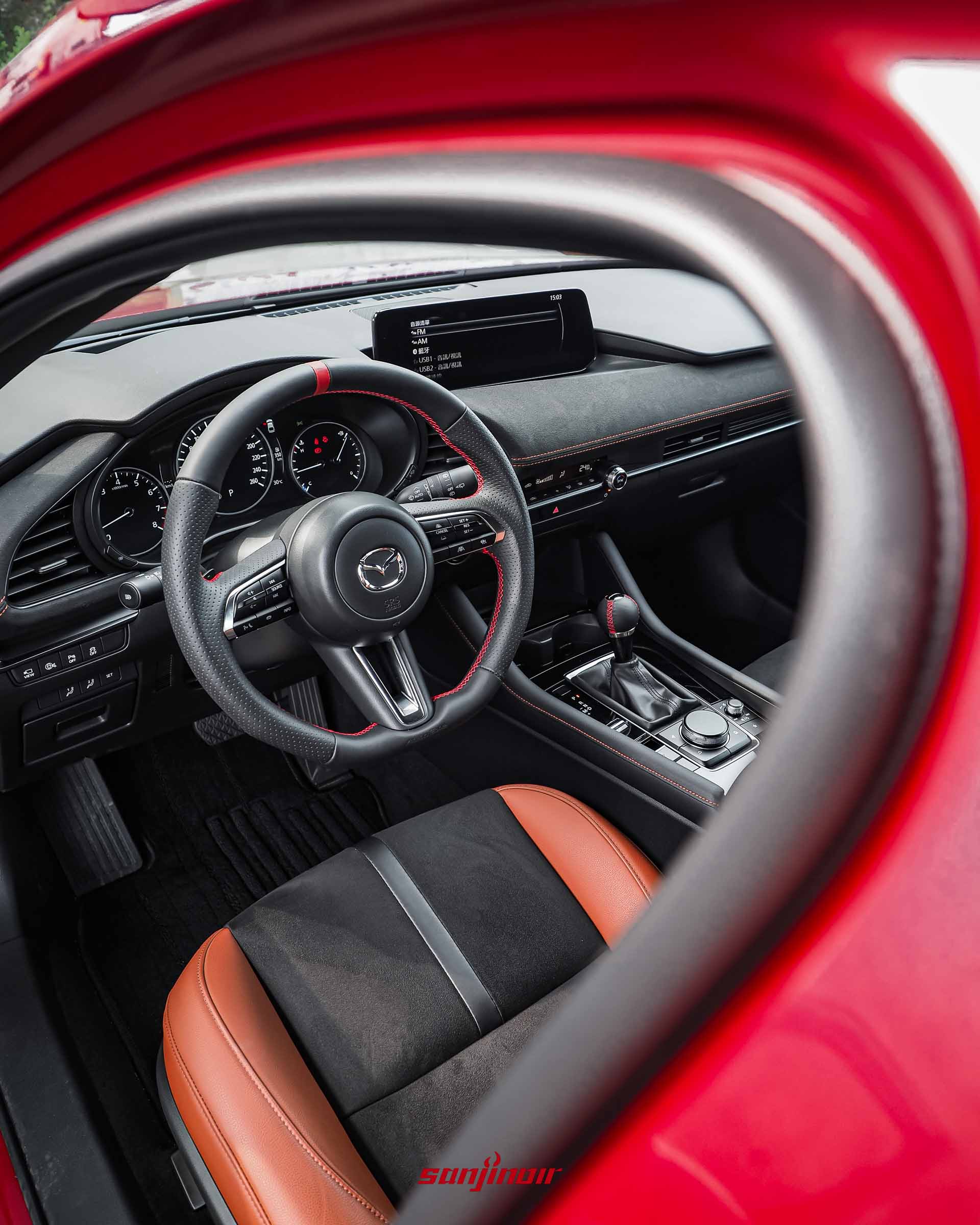 從副駕駛側看MAZDA3 HOMURA內裝，AutoExe NAPPA運動化平底方向盤有紅色中心標記和縫線，中控台有大螢幕。