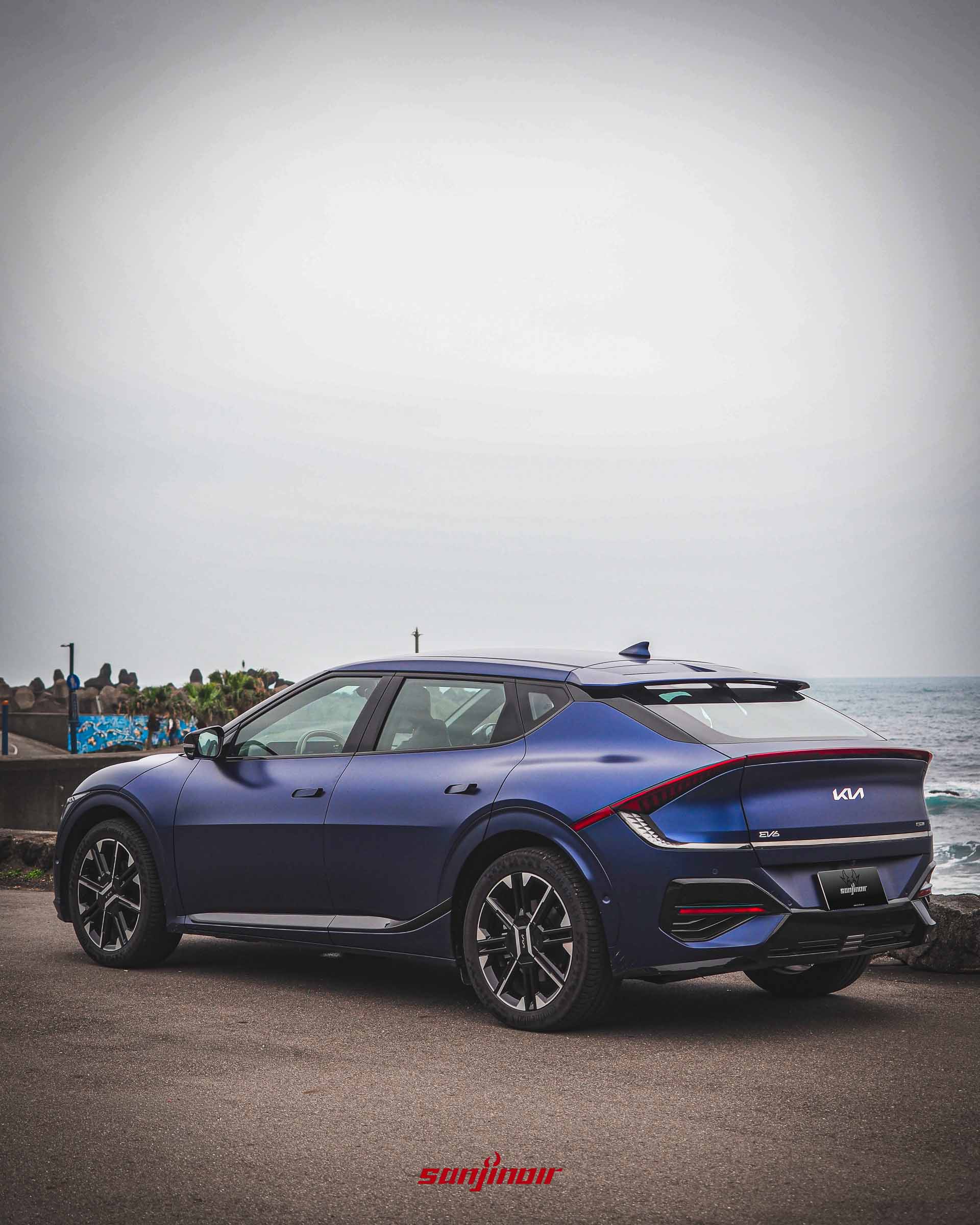 藍色啞光Kia EV6 GT-Line電動車車尾3/4視角照片，展示橫貫式尾燈和GT-Line後保險桿細節。